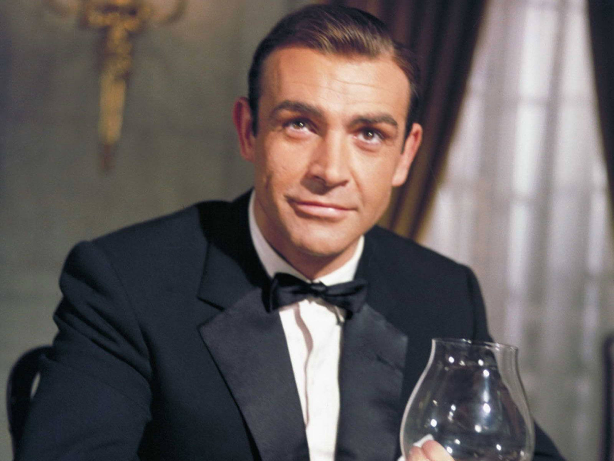 Sean Connery 桌布 壁紙 — 一位穿著黑色燕尾服的時尚男士在優雅的房間裡自信地拿著酒杯。