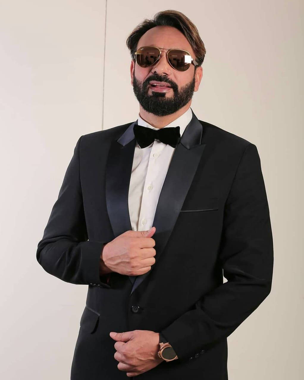 Celebrity 桌布 壁紙 — 一位穿著黑色禮服和太陽眼鏡的時尚男士在純白色背景前自信地擺姿勢。