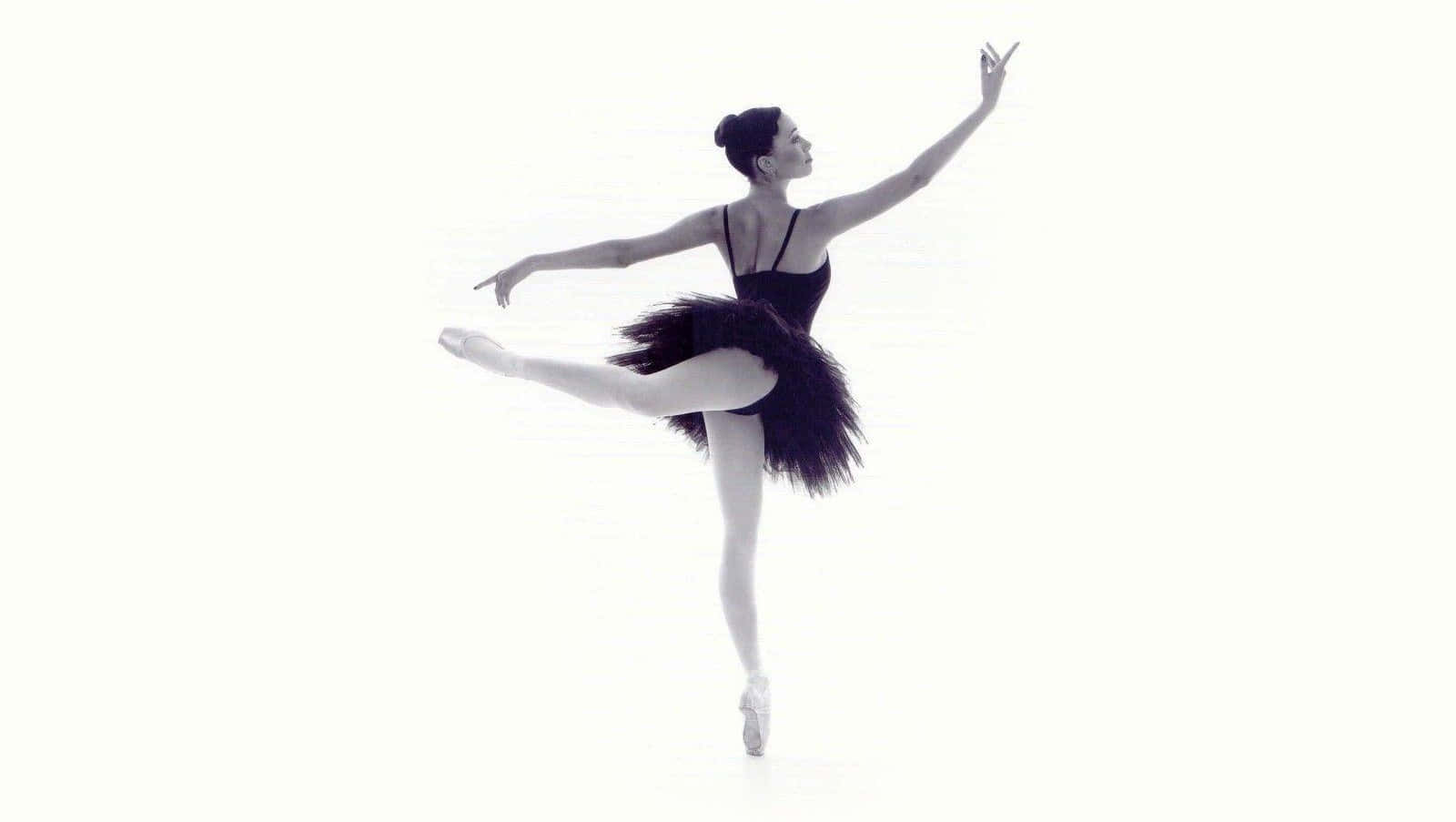 Ballet Dancer 桌布 壁紙 — 一位穿著黑色芭蕾舞裙的芭蕾舞者，在純白背景前優雅地踮起腳尖保持平衡。
