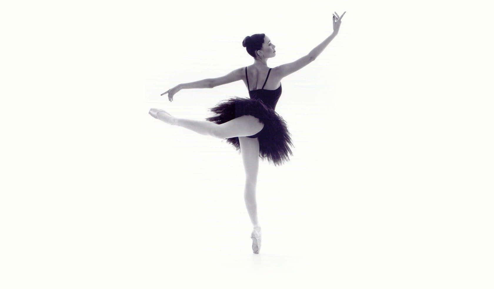 Ballet 桌布 壁紙 — 一位穿著黑色芭蕾舞裙的芭蕾舞者，在純白背景前優雅地踮起腳尖保持平衡。