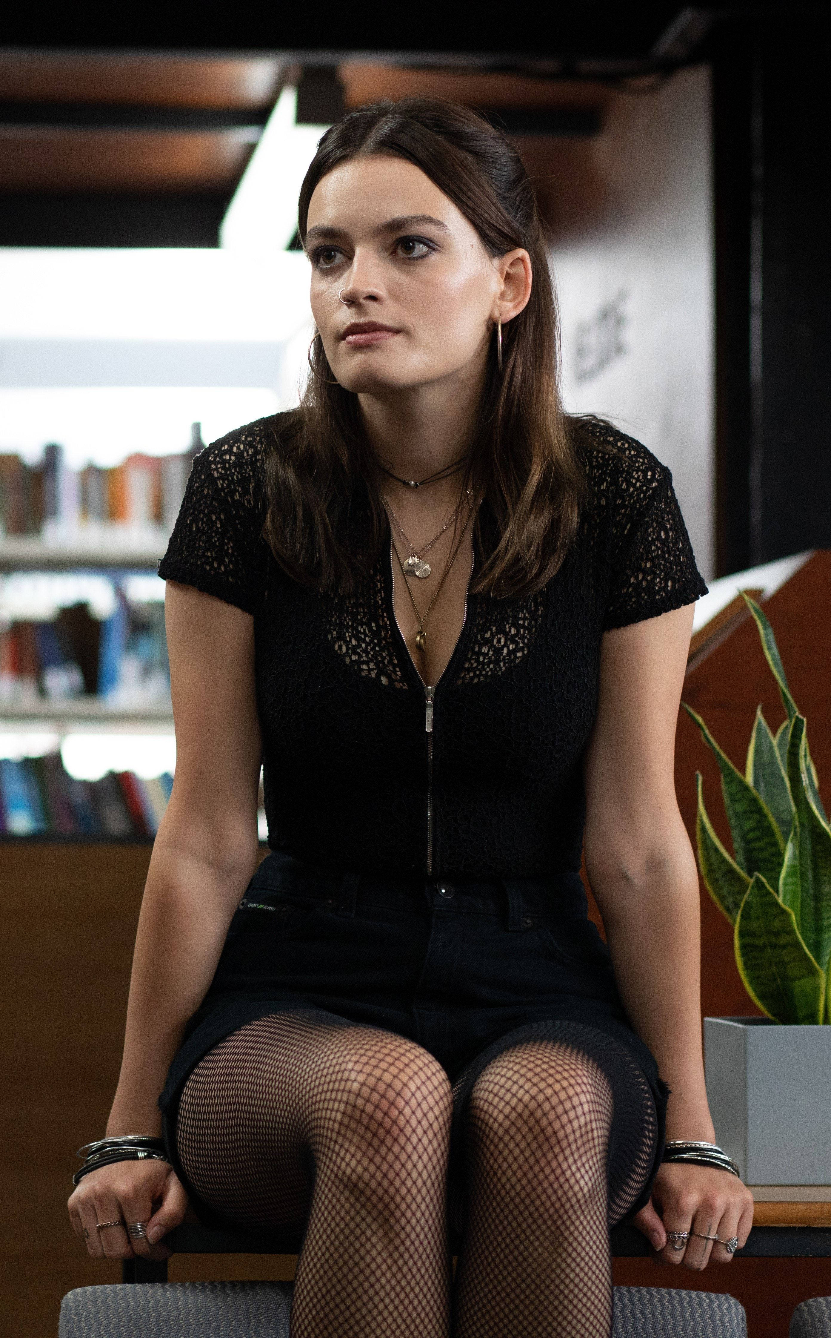 Emma 桌布 壁紙 — 一位穿著黑色蕾絲上衣和漁網襪的女性，在現代圖書館環境中若有所思地坐在椅子上。