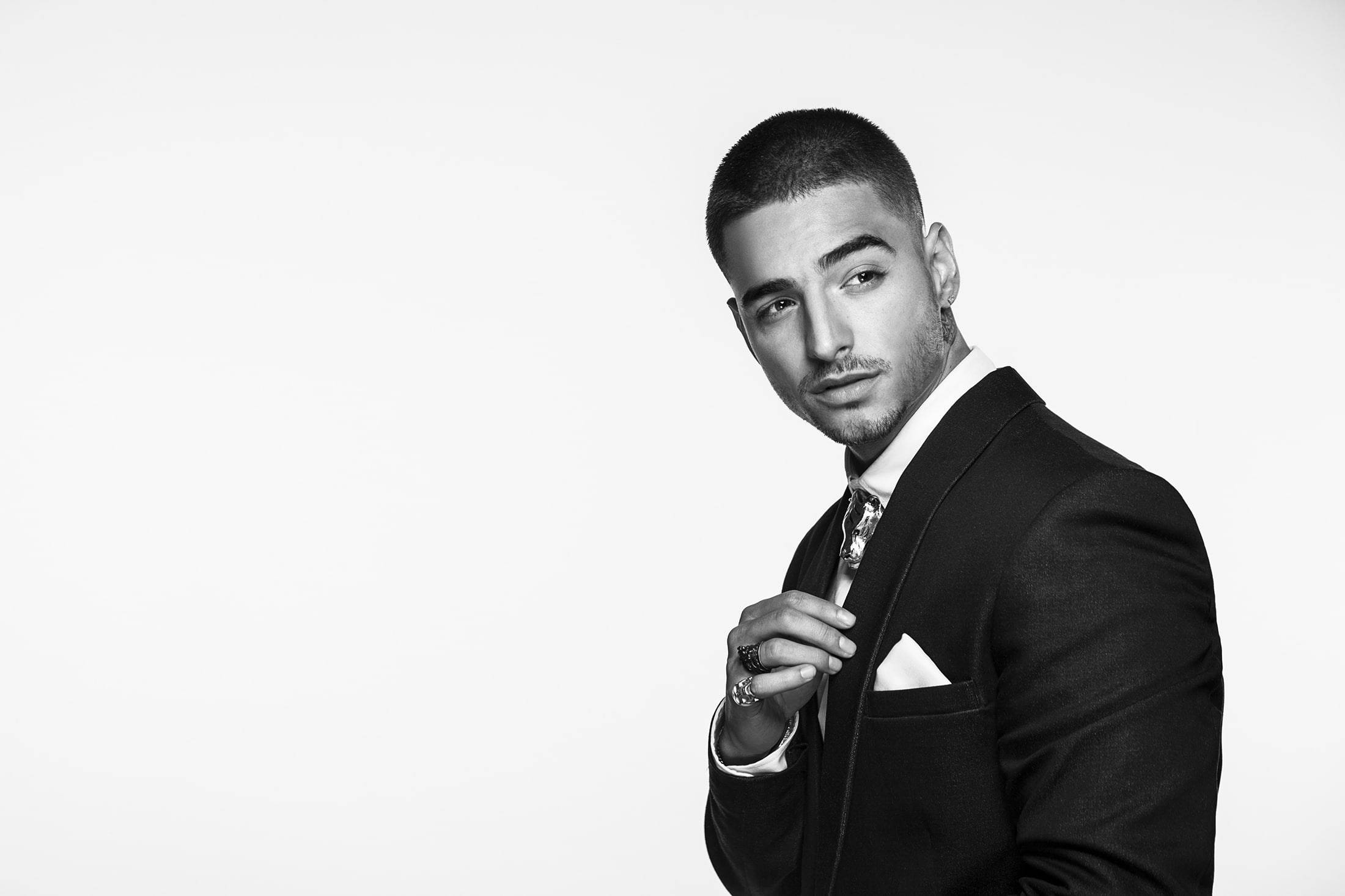 Maluma 桌布 壁紙 — 一位穿著黑色西裝、打扮俐落的男士，在純白背景前自信擺姿勢的黑白肖像。