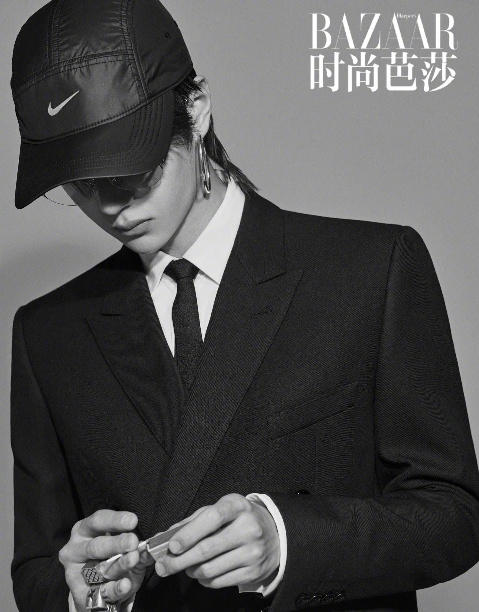 王一博 桌布 壁紙 — 一位穿著黑色西裝和帽子的時尚男士，在純灰色背景前專注地握著剃刀刀片。