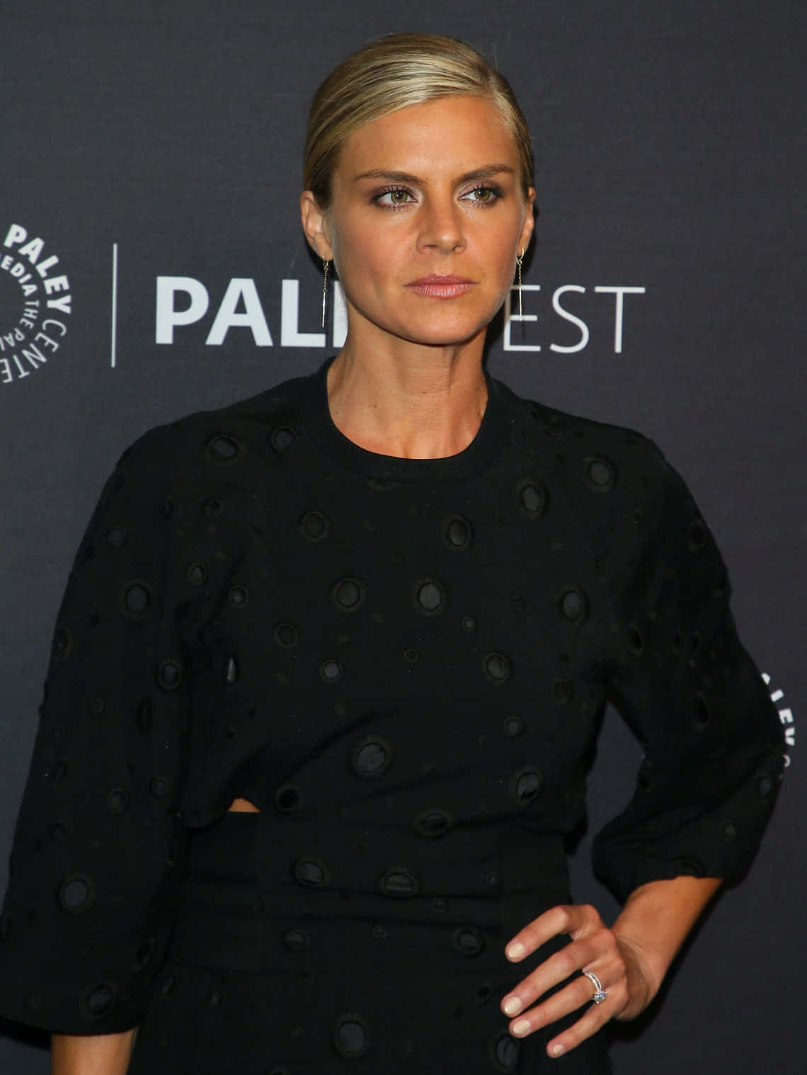 eliza coupe 桌布 壁紙 — 一位穿著黑色質感連衣裙的優雅女士，在深色背景的Paley Center活動中自信地站立。