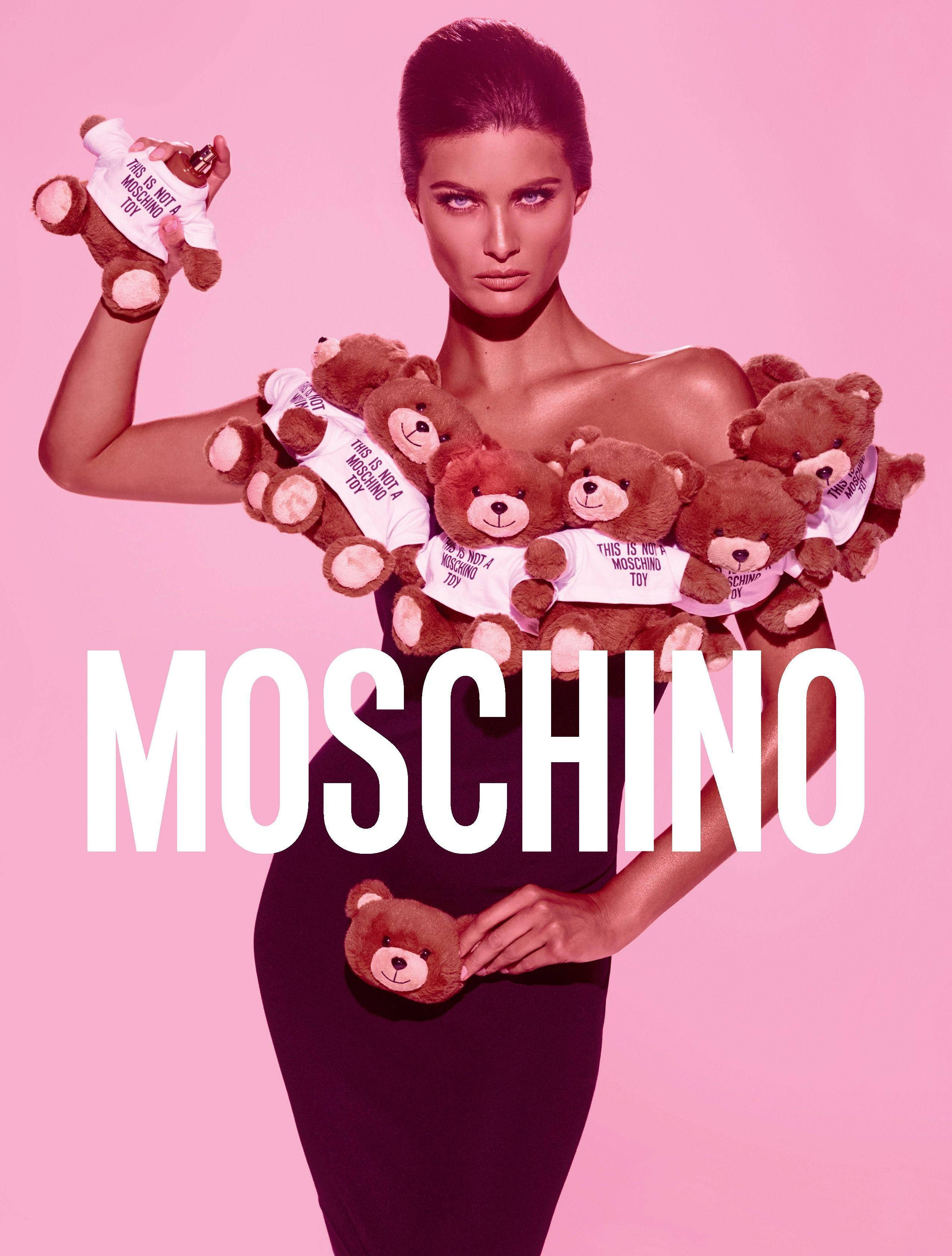 moschino 桌布 壁紙 — 一位穿著黑色連衣裙的模特兒在粉紅色背景前抱著穿著「this is not a moschino toy」襯衫的泰迪熊。