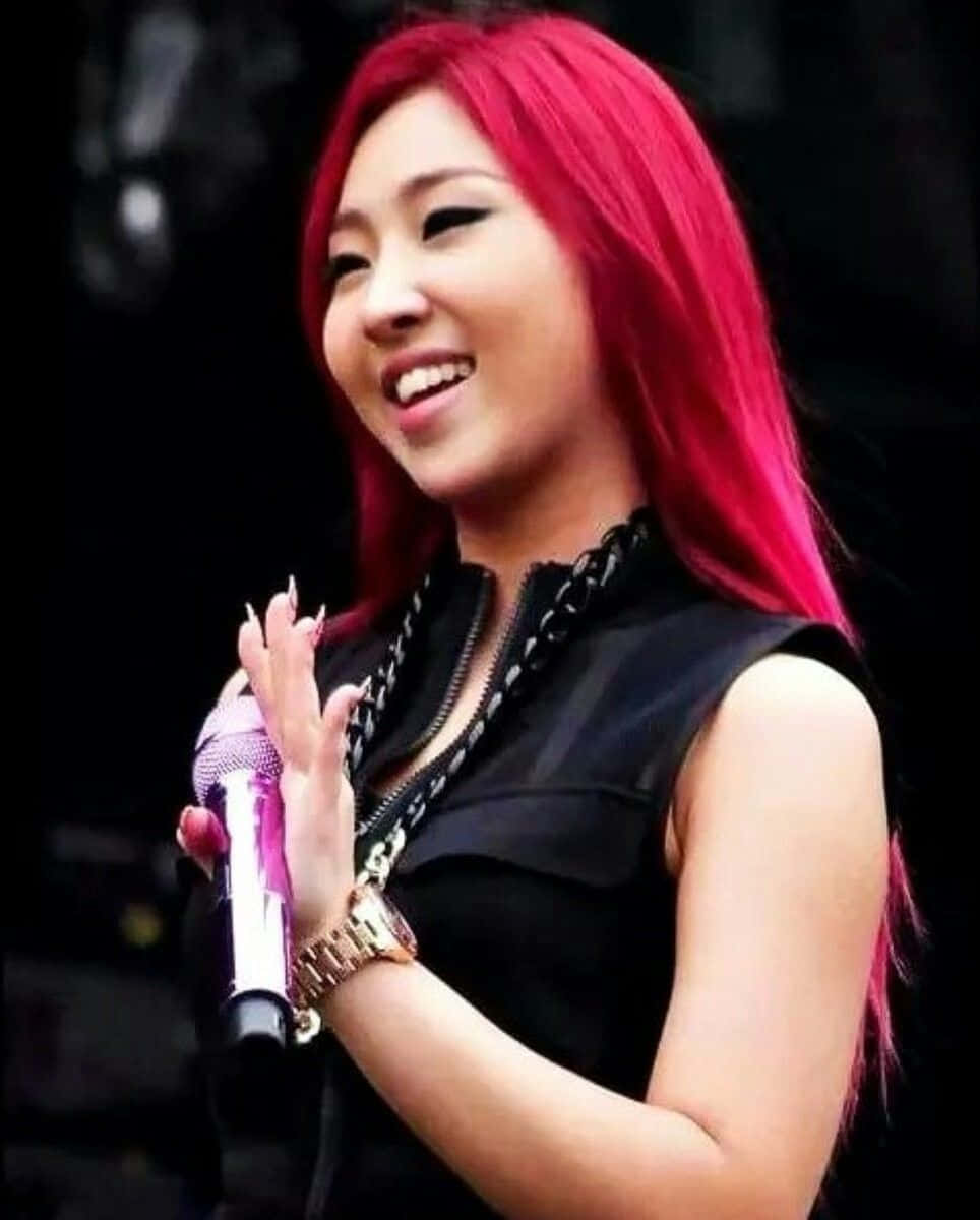 2ne1 桌布 壁紙 — 一位笑容滿面、擁有鮮豔紅髮的女性，手持麥克風，身穿黑色無袖上衣和金色手錶。