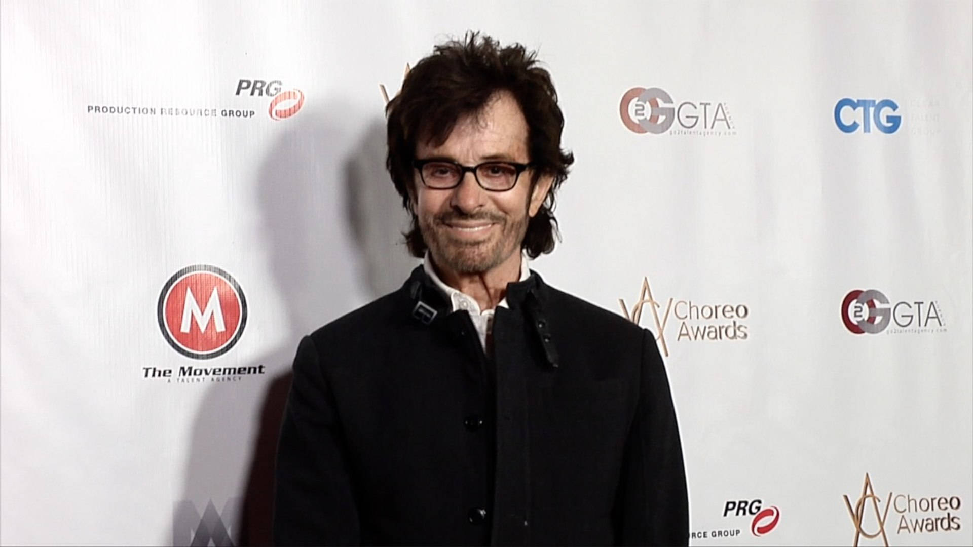 actor 桌布 壁紙 — 一位笑容滿面、深色頭髮、戴眼鏡的男士，在帶有標誌的白色背景前穿著黑色外套。