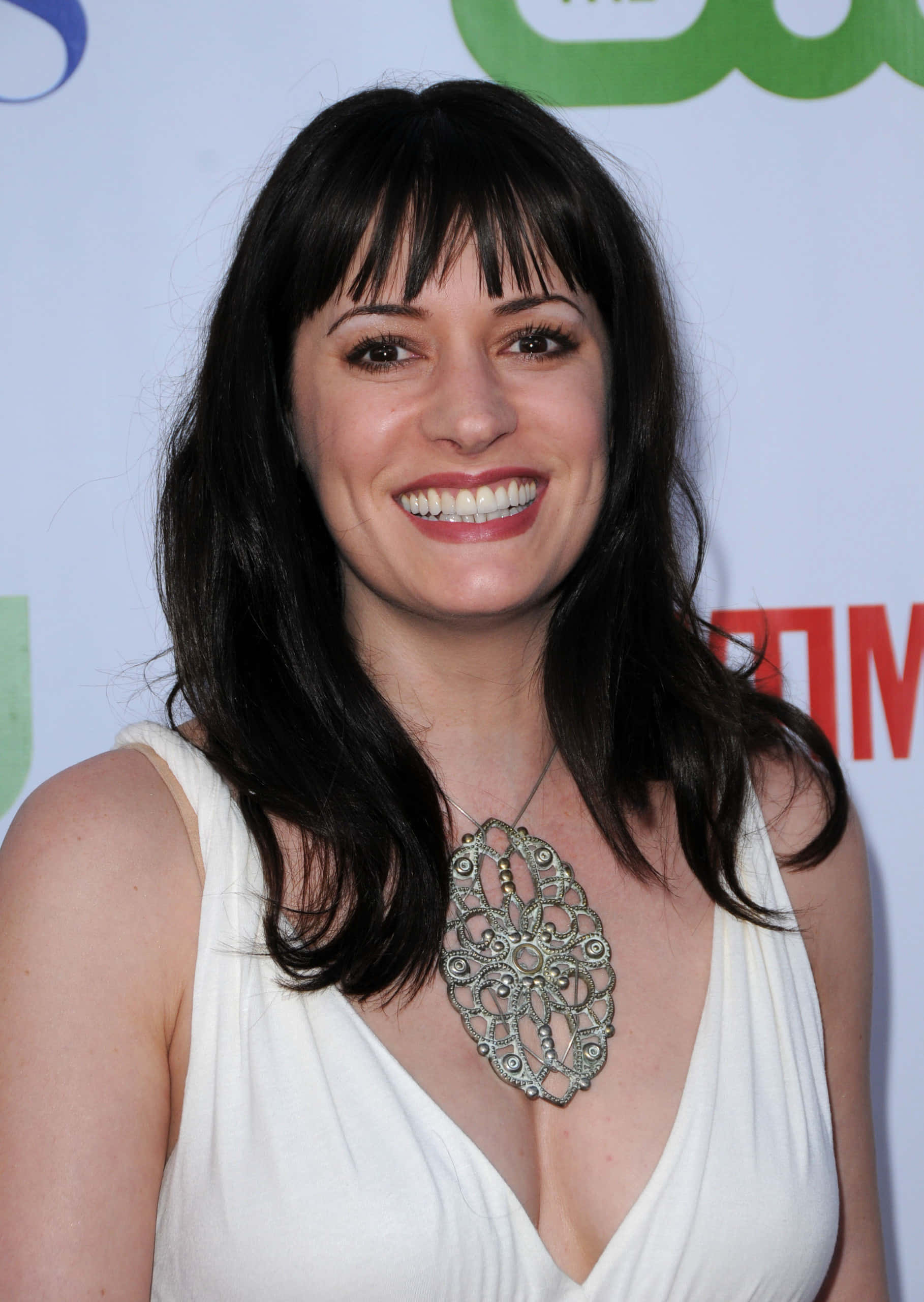 paget brewster 桌布 壁紙 — 一位笑容滿面、深色頭髮和瀏海的女士，在紅地毯活動中穿著白色連衣裙和華麗的銀項鍊。
