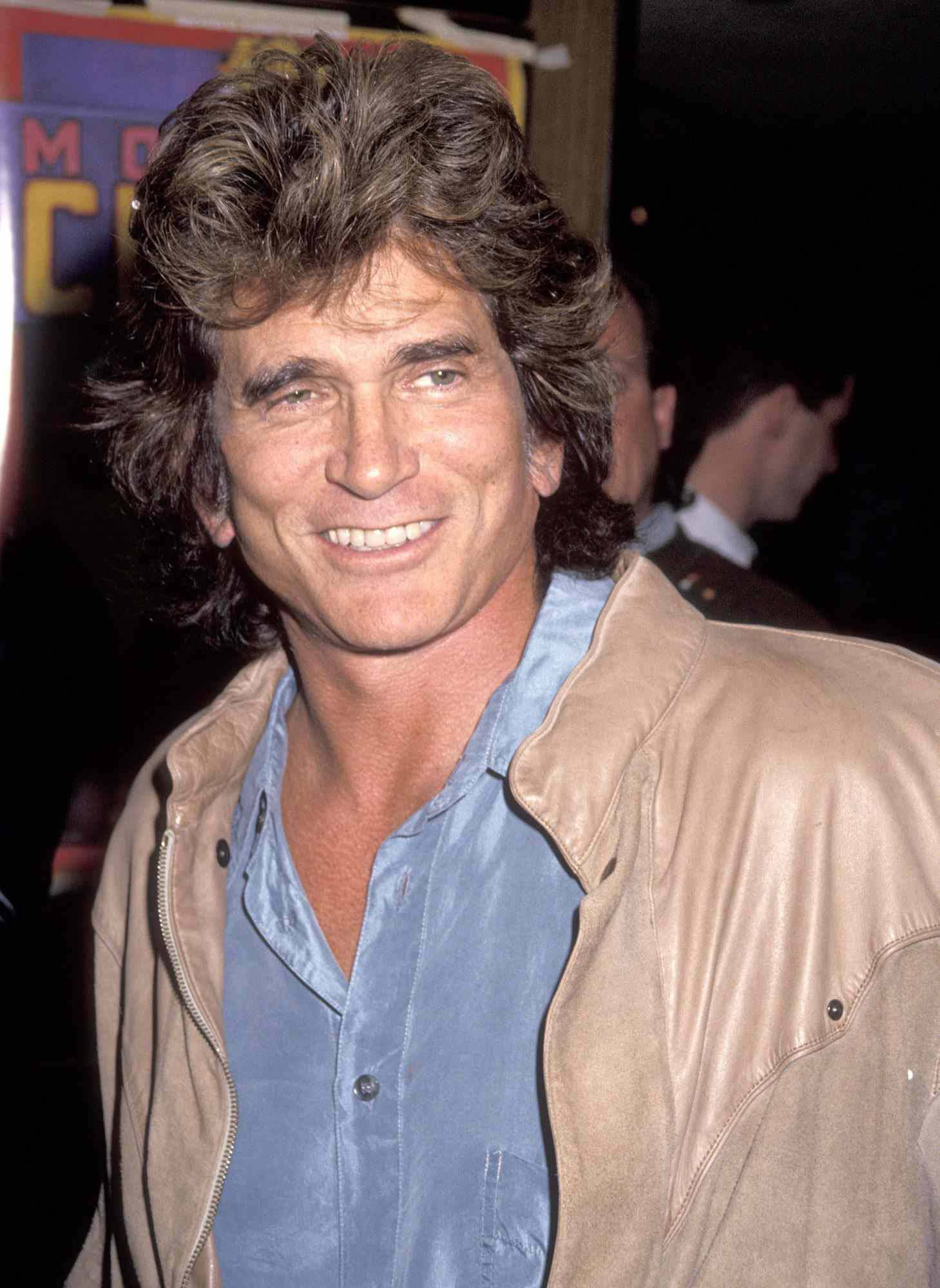 Michael Landon 桌布 壁紙 — 一位笑容滿面、頭髮濃密的男士在燈光昏暗的活動中，身穿藍色襯衫外搭棕褐色皮夾克。