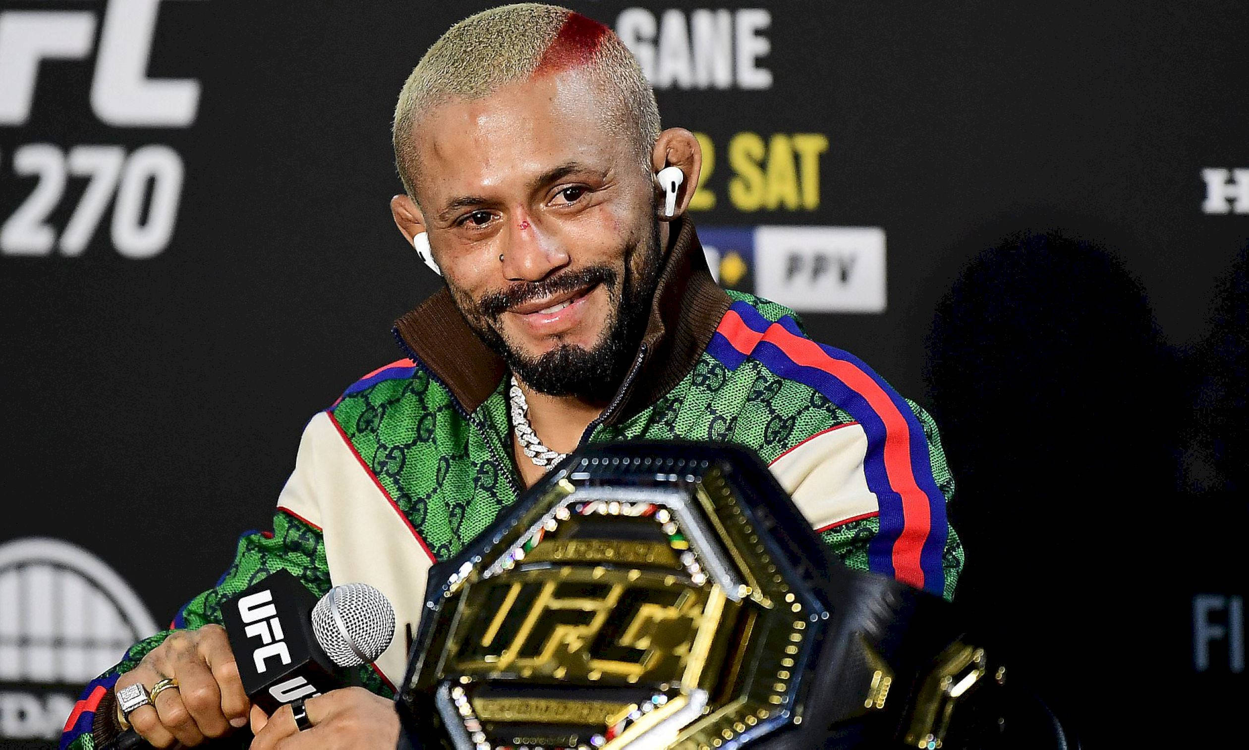 UFC 桌布 壁紙 — 一位笑容滿面的UFC拳手，頭髮上有一條紅色挑染，在記者會上手持冠軍腰帶和麥克風。