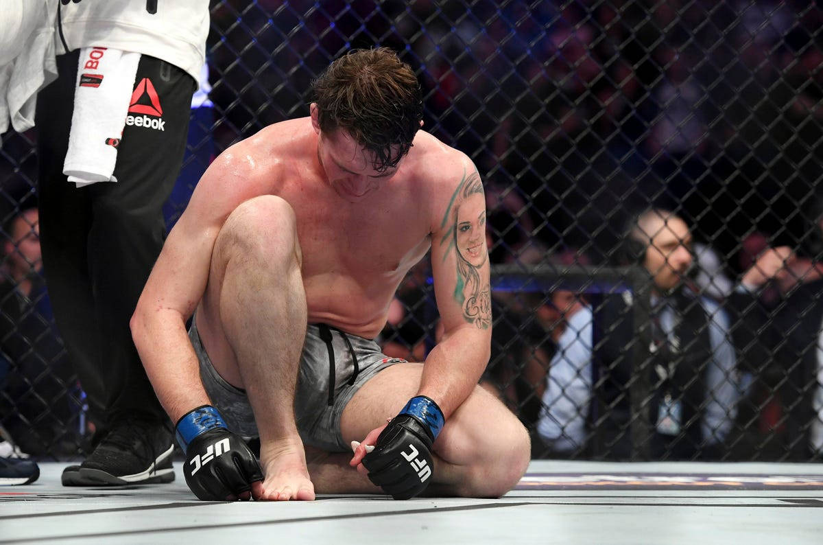 UFC 桌布 壁紙 — 一位筋疲力盡的綜合格鬥選手在比賽後跪在八角籠地上，低著頭，露出有刺青的手臂。