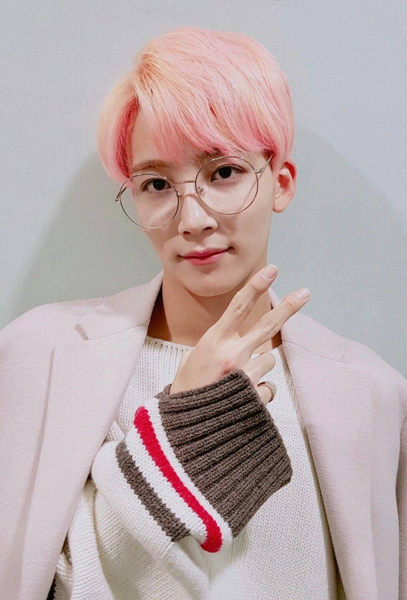 yoon jeonghan 桌布 壁紙 — 一位粉紅色頭髮、戴眼鏡的年輕男子，穿著柔和的粉彩服裝，微笑著做出和平手勢。