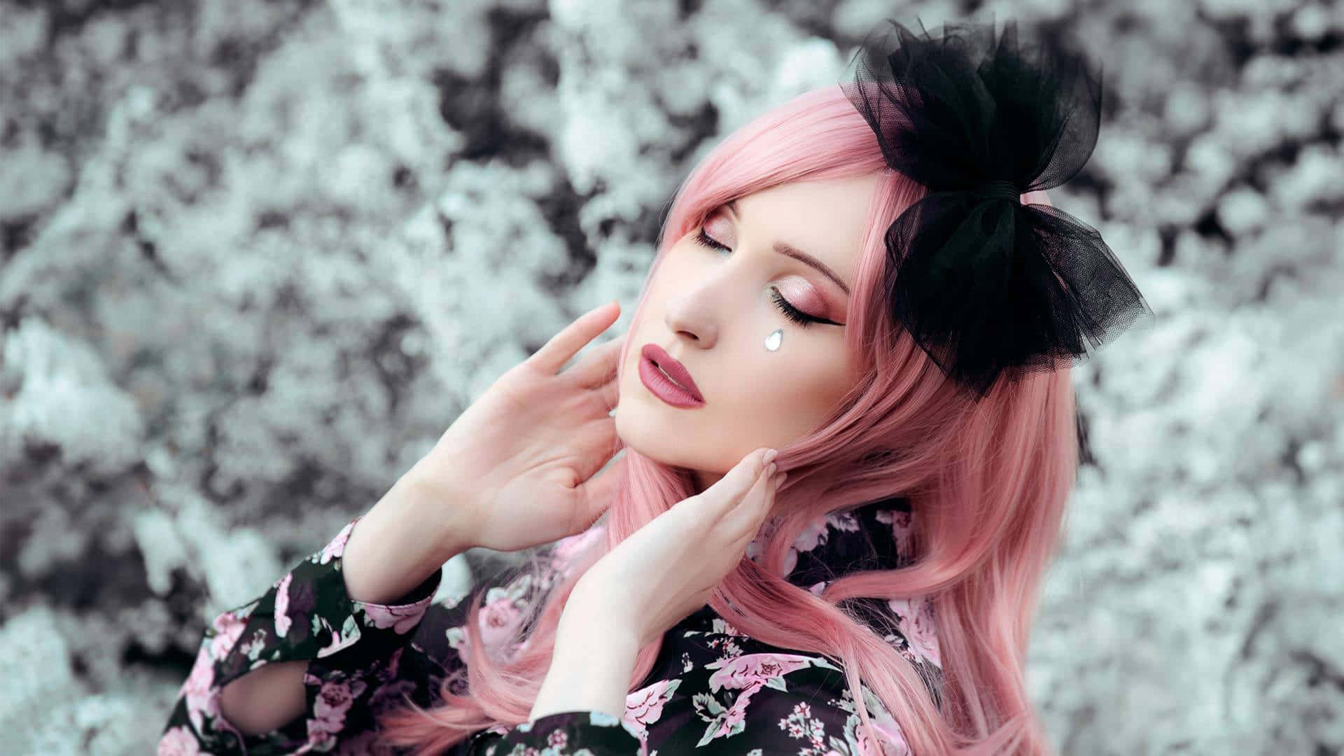 Goth 桌布 壁紙 — 一位粉紅色頭髮、戴著黑色蝴蝶結的女性，在雪景背景下，閉著眼睛，淚水滴落，輕輕觸摸臉龐。