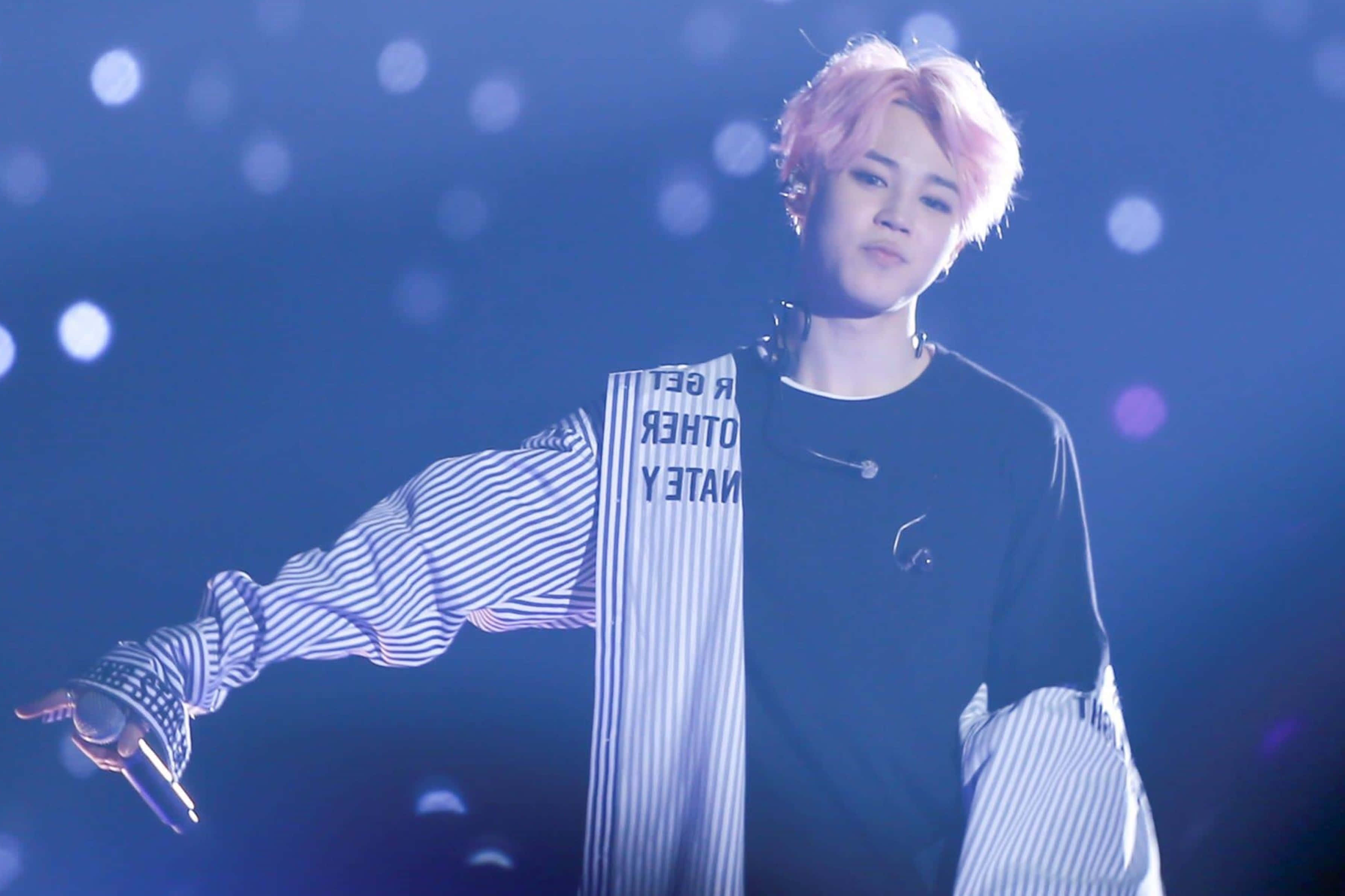 Bts Jimin 桌布 壁紙 — 一位粉紅色頭髮、條紋袖子的表演者在藍色燈光、散景燈光的舞台上做手勢。