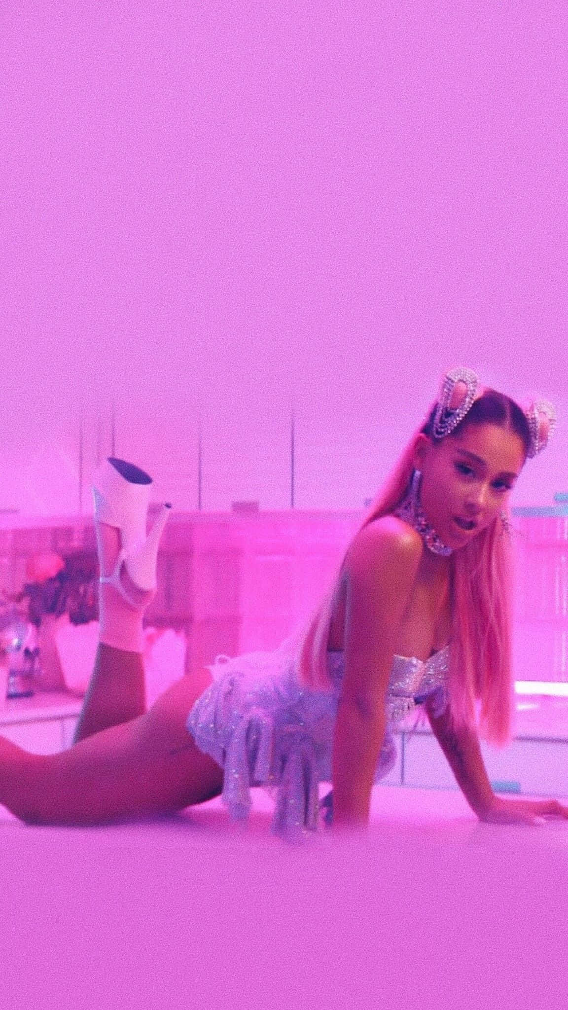 Ariana Grande 7 Rings 桌布 壁紙 — 一位粉紅色頭髮、穿著閃亮服裝的女性在粉紅色屋頂上，在霓虹粉紅燈光下擺姿勢。