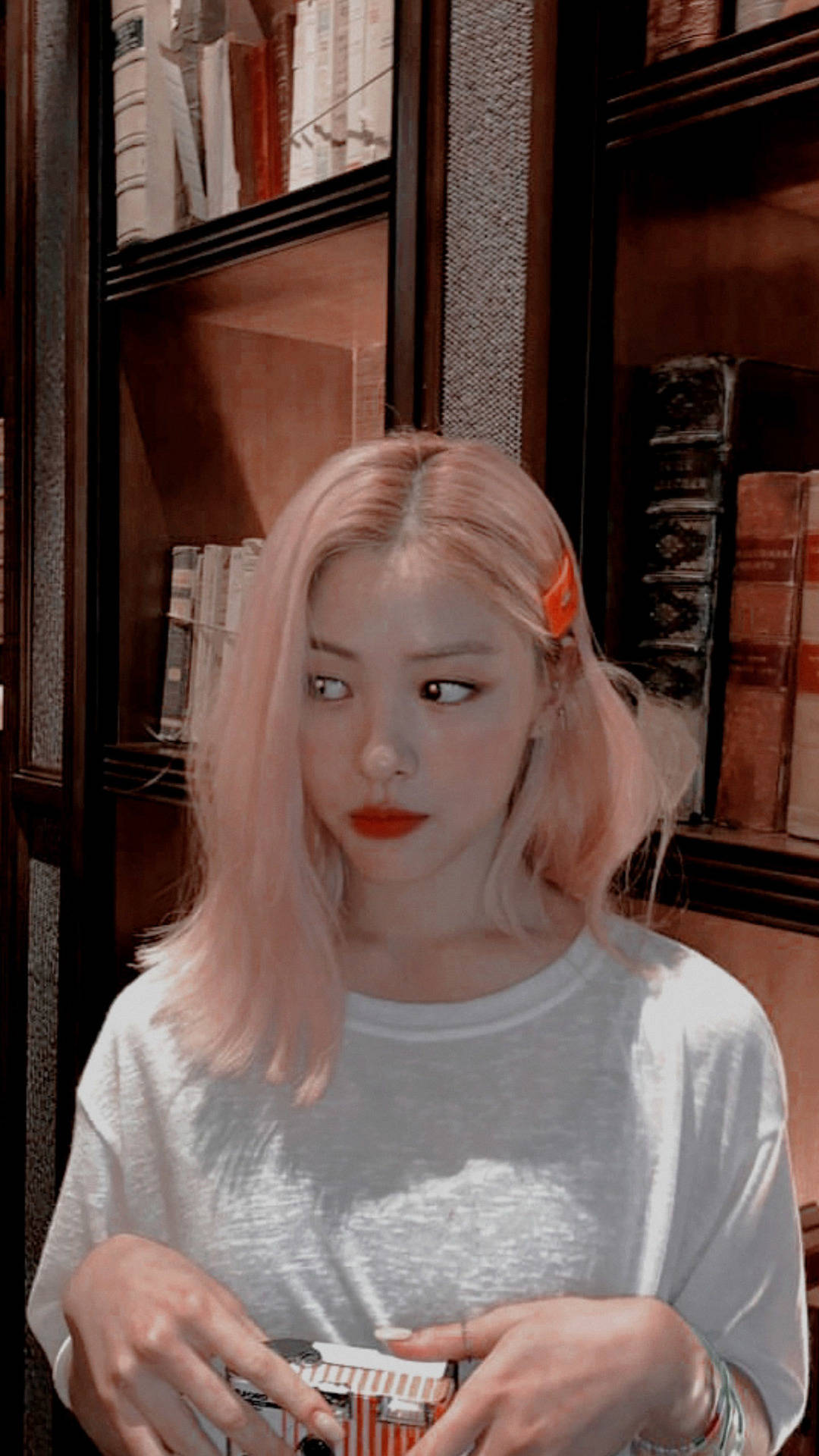ITZY 桌布 壁紙 — 一位粉紅色頭髮、紅唇的年輕女性在裝滿書本的深色木書架前拿著一個盒子。