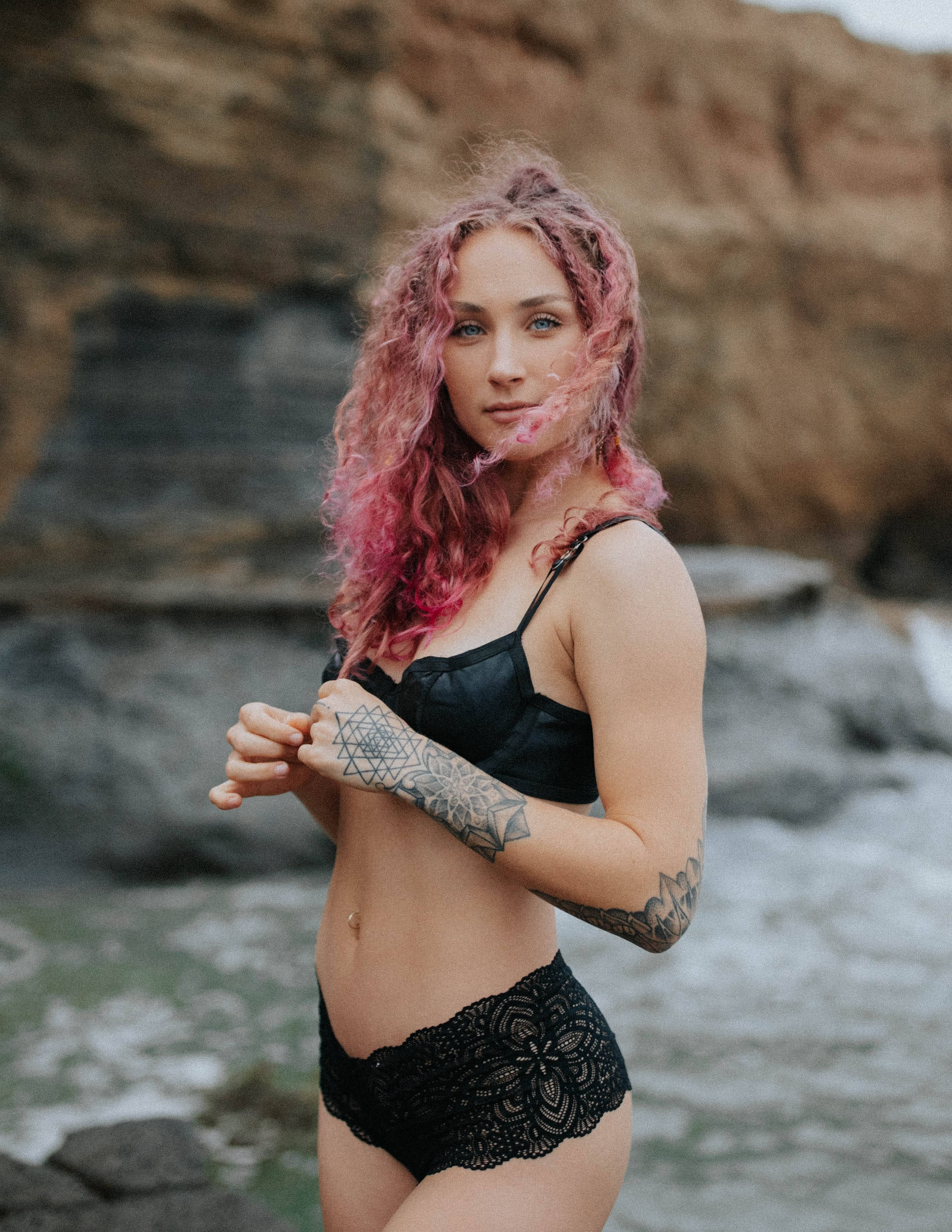 Sexy 桌布 壁紙 — 一位粉紅色頭髮和刺青的女性站在岩石峭壁旁，海浪在她身後拍打。