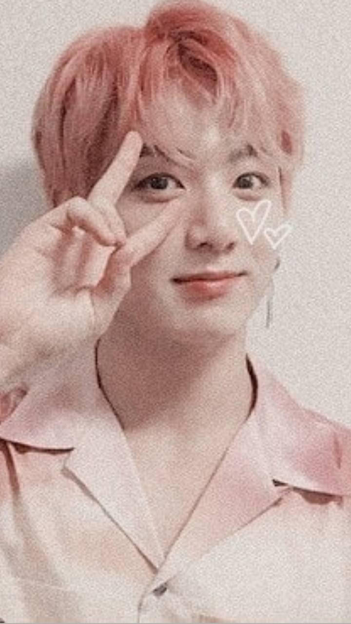 Jungkook Aesthetic 桌布 壁紙 — 一位粉紅色頭髮和襯衫的年輕男子在眼睛附近做出和平手勢，心形漂浮在他的臉旁。