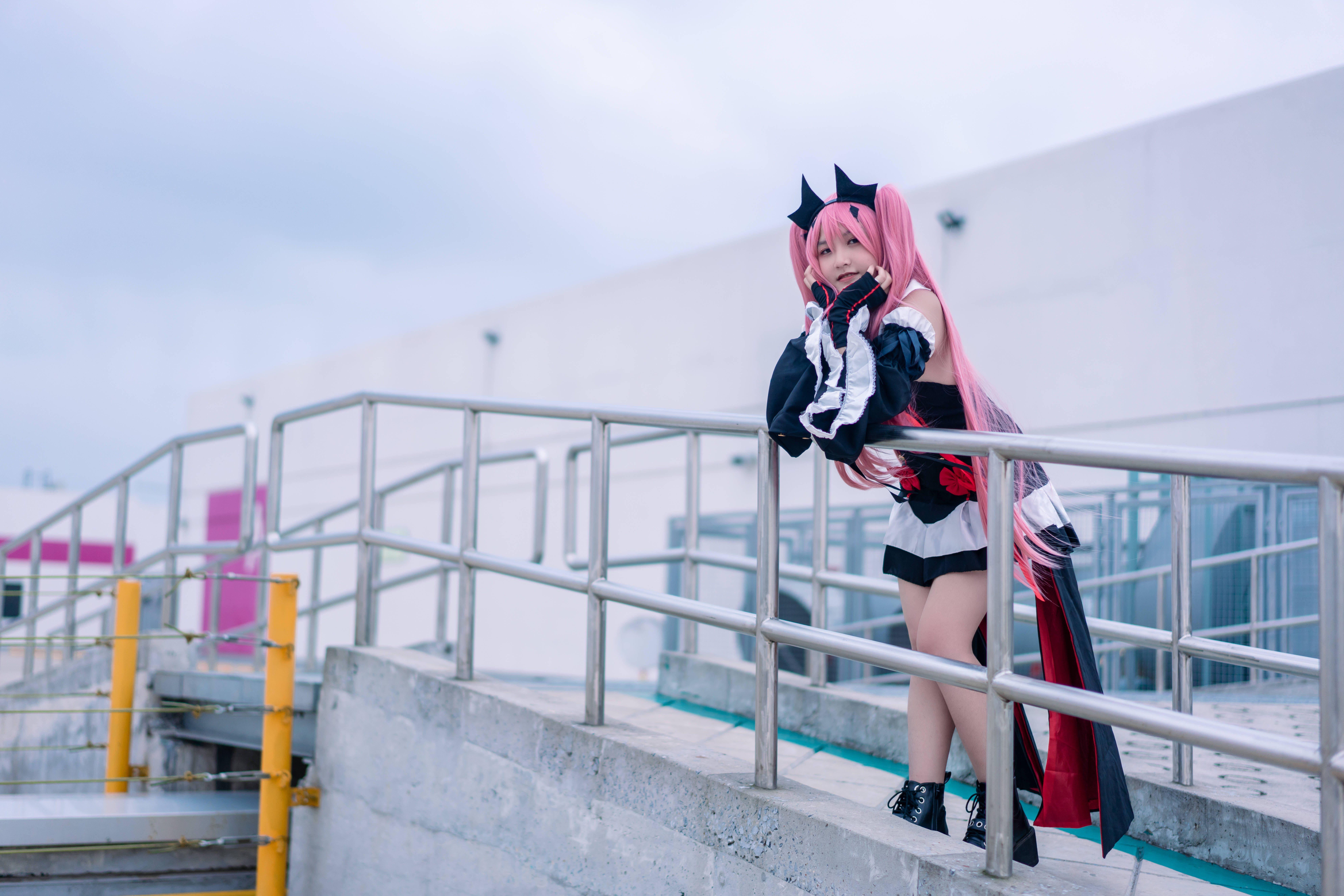 動漫女孩 桌布 壁紙 — 一位粉紅色頭髮的cosplayer穿著黑白配紅色點綴的服裝，靠著金屬欄杆，背景是陰天。