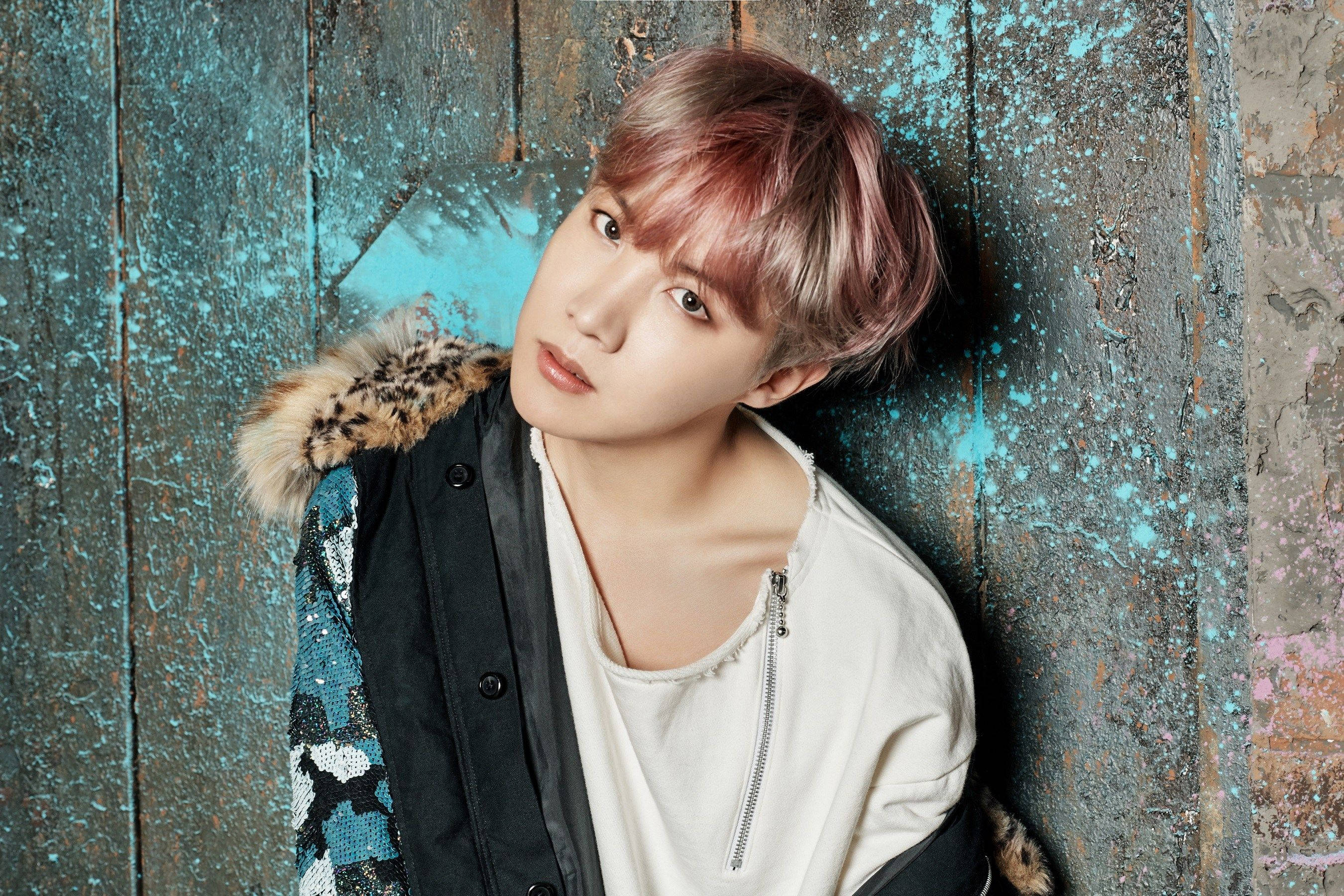 jhope 桌布 壁紙 — 一位粉紅色頭髮的年輕人靠著風化的藍色木牆，身穿帶有豹紋毛邊的夾克。