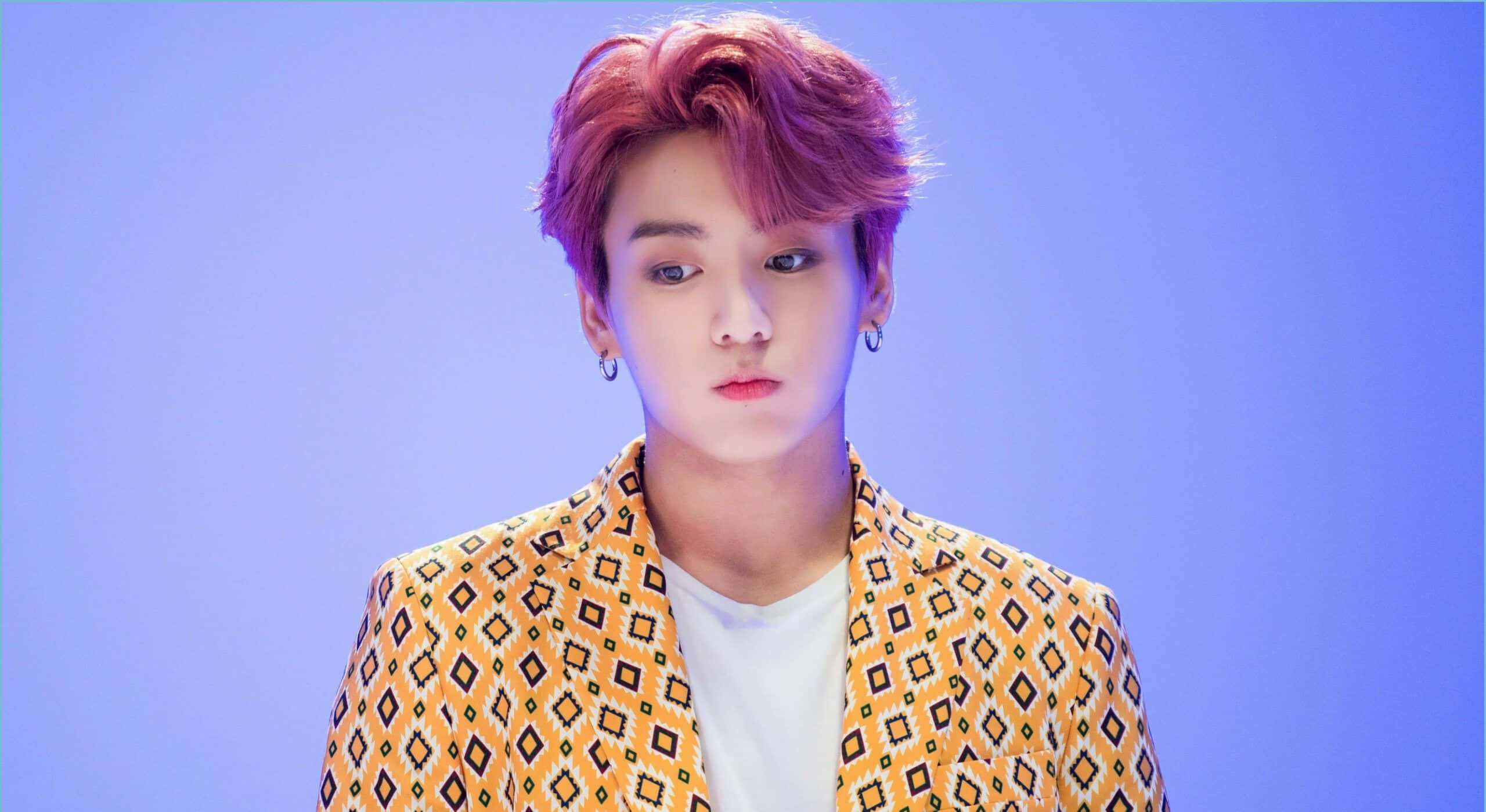 Jungkook 桌布 壁紙 — 一位粉紅色頭髮的年輕男子穿著圖案黃色西裝外套，背景為純藍色。