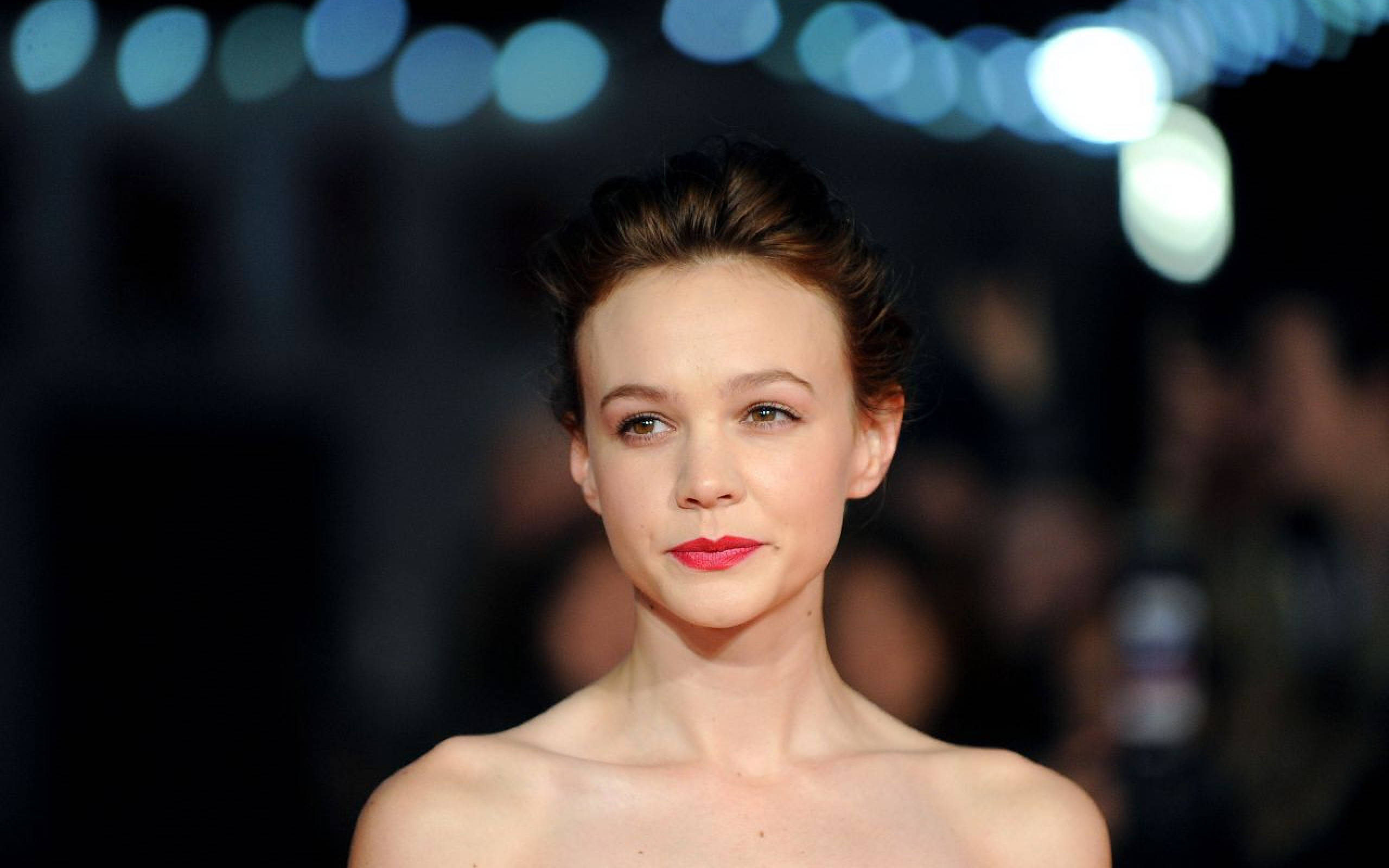 Carey Mulligan 桌布 壁紙 — 一位紅唇、造型頭髮的女性，在模糊的藍色發光背景前平靜地凝視。