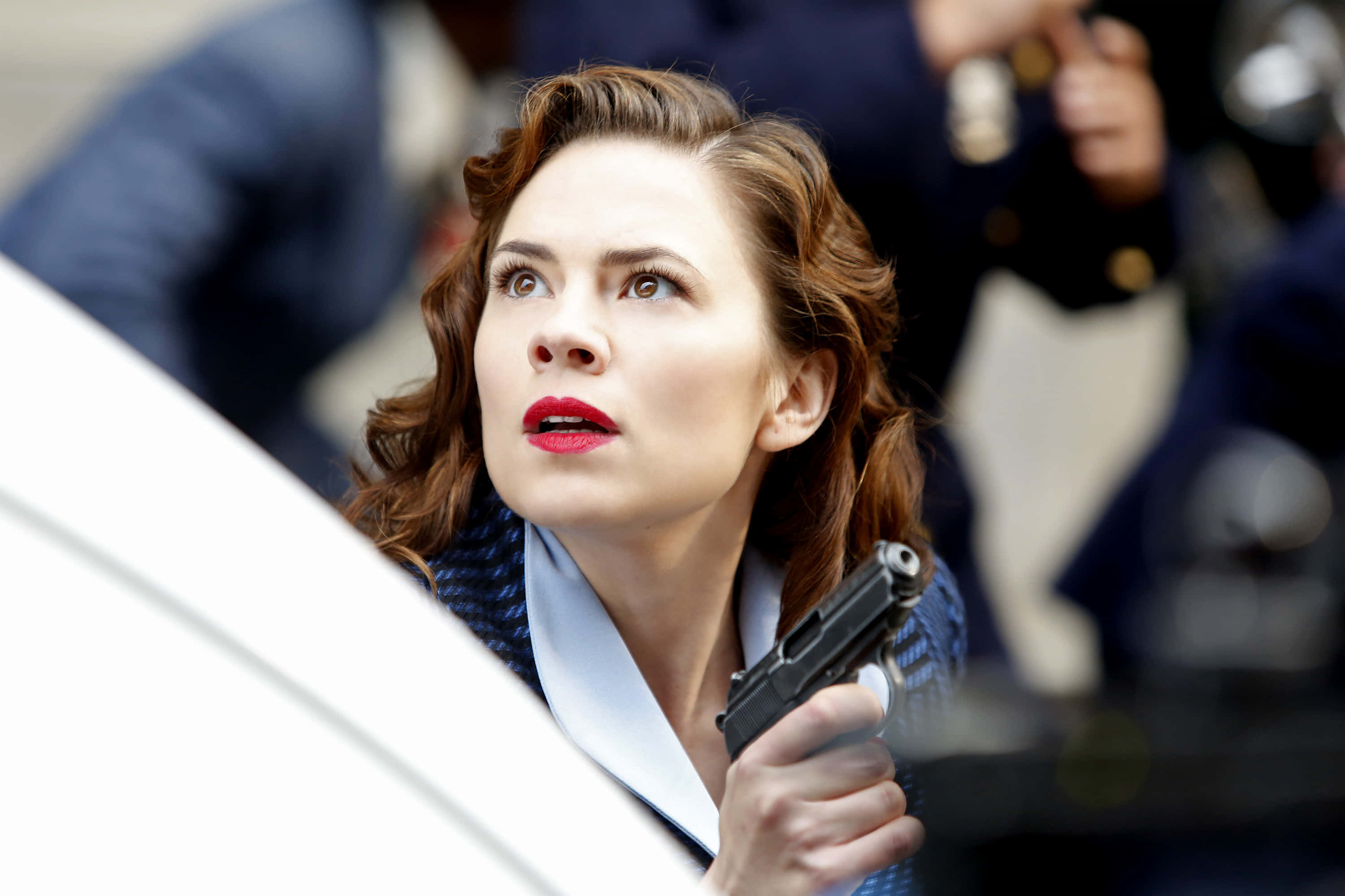 Peggy Carter 桌布 壁紙 — 一位紅唇捲髮的女性手持手槍，向上凝視，神情專注。