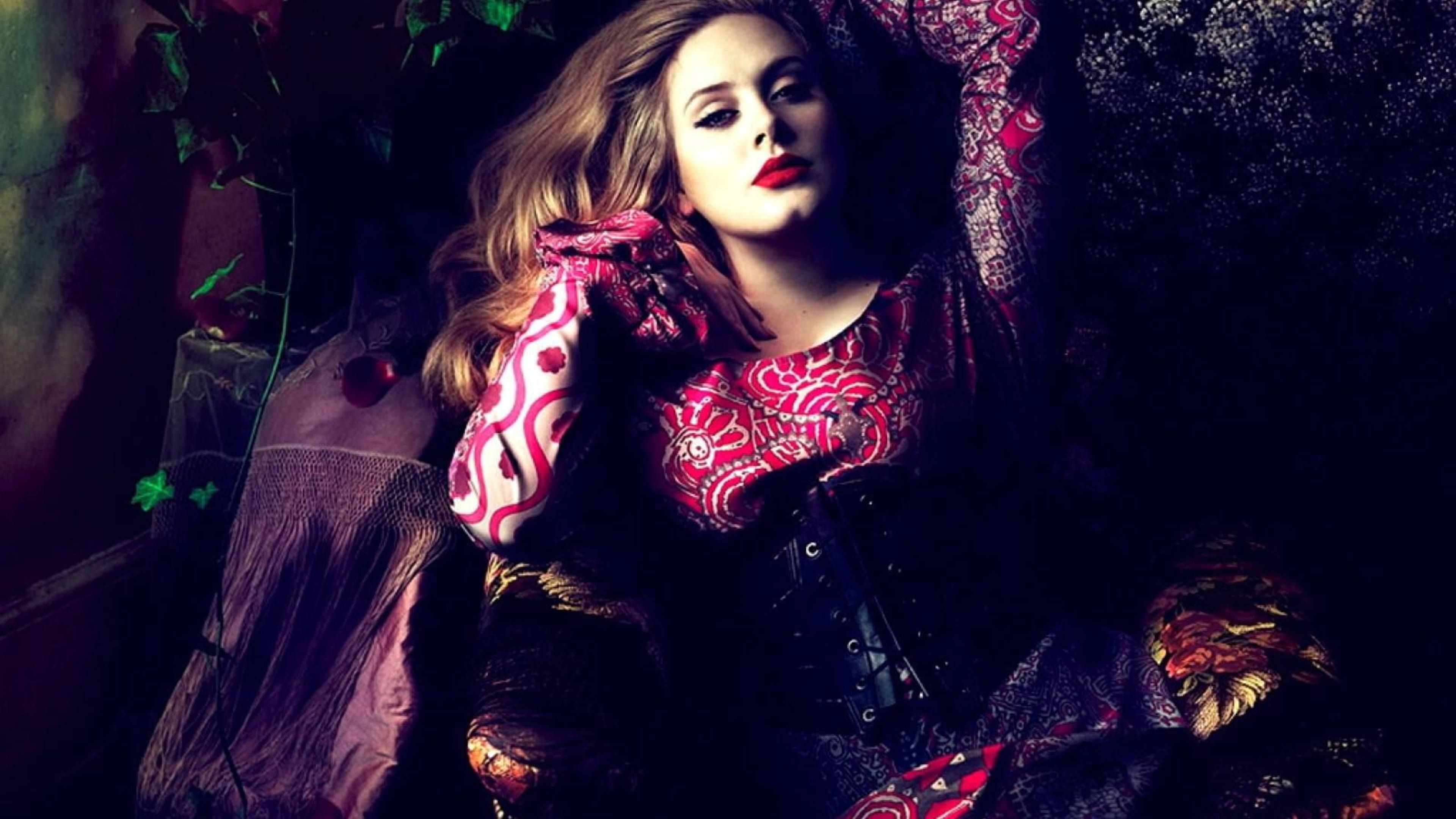 Adele 桌布 壁紙 — 一位紅唇長髮的女性在陰影中、裝飾華麗的環境中斜倚，周圍有常春藤和華麗的布料。