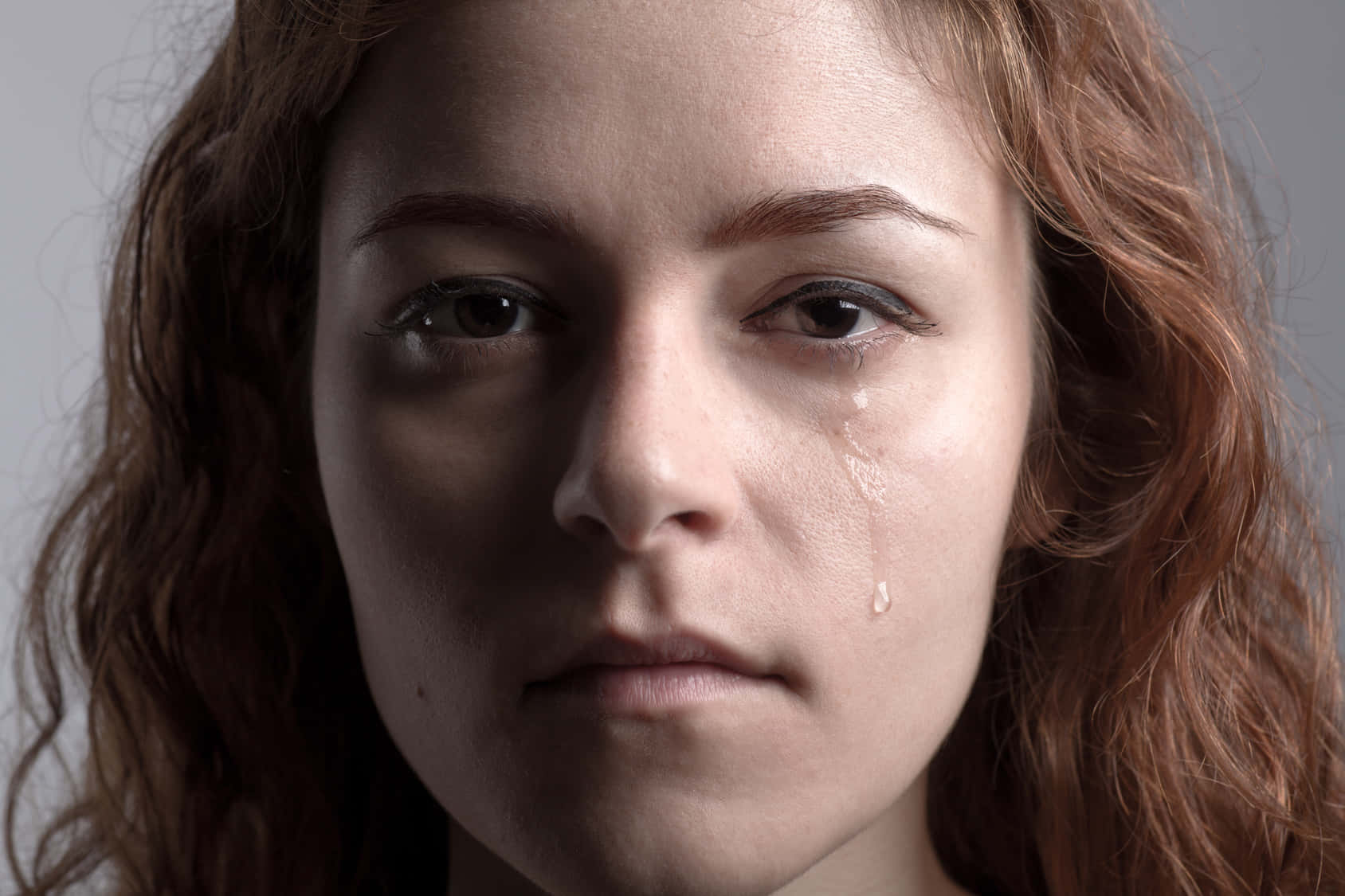 cry 桌布 壁紙 — 一位紅棕色頭髮女性的特寫肖像，一滴淚水順著臉頰流下，背景為中性灰色。