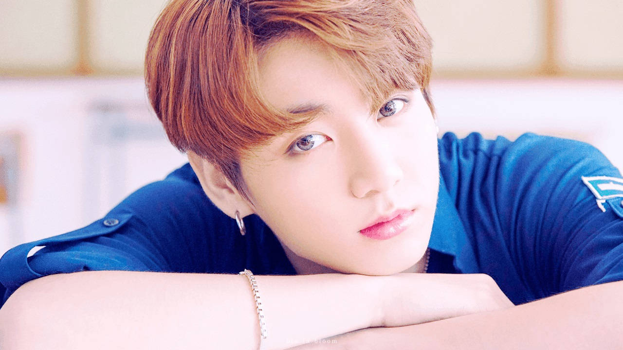 Cute Bts 桌布 壁紙 — 一位紅褐色頭髮的年輕男子，身穿藍色襯衫和銀飾，將下巴擱在手臂上。