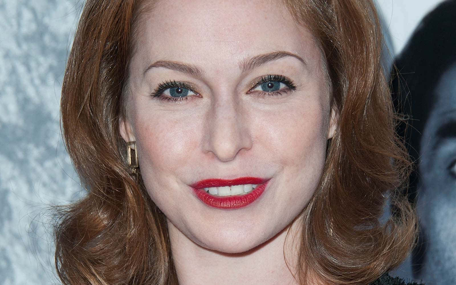 Esmé Bianco 桌布 壁紙 — 一位紅髮、塗著大膽紅唇膏的女性，對著鏡頭溫暖微笑的特寫肖像。