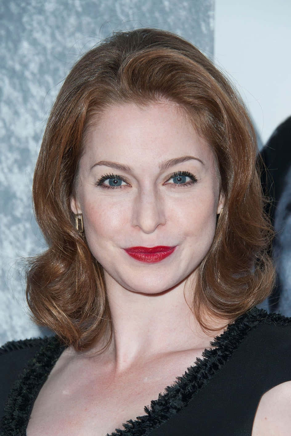Esmé Bianco 桌布 壁紙 — 一位紅髮、塗著大膽紅唇膏的女性，在紋理灰色背景前溫柔微笑的特寫肖像。
