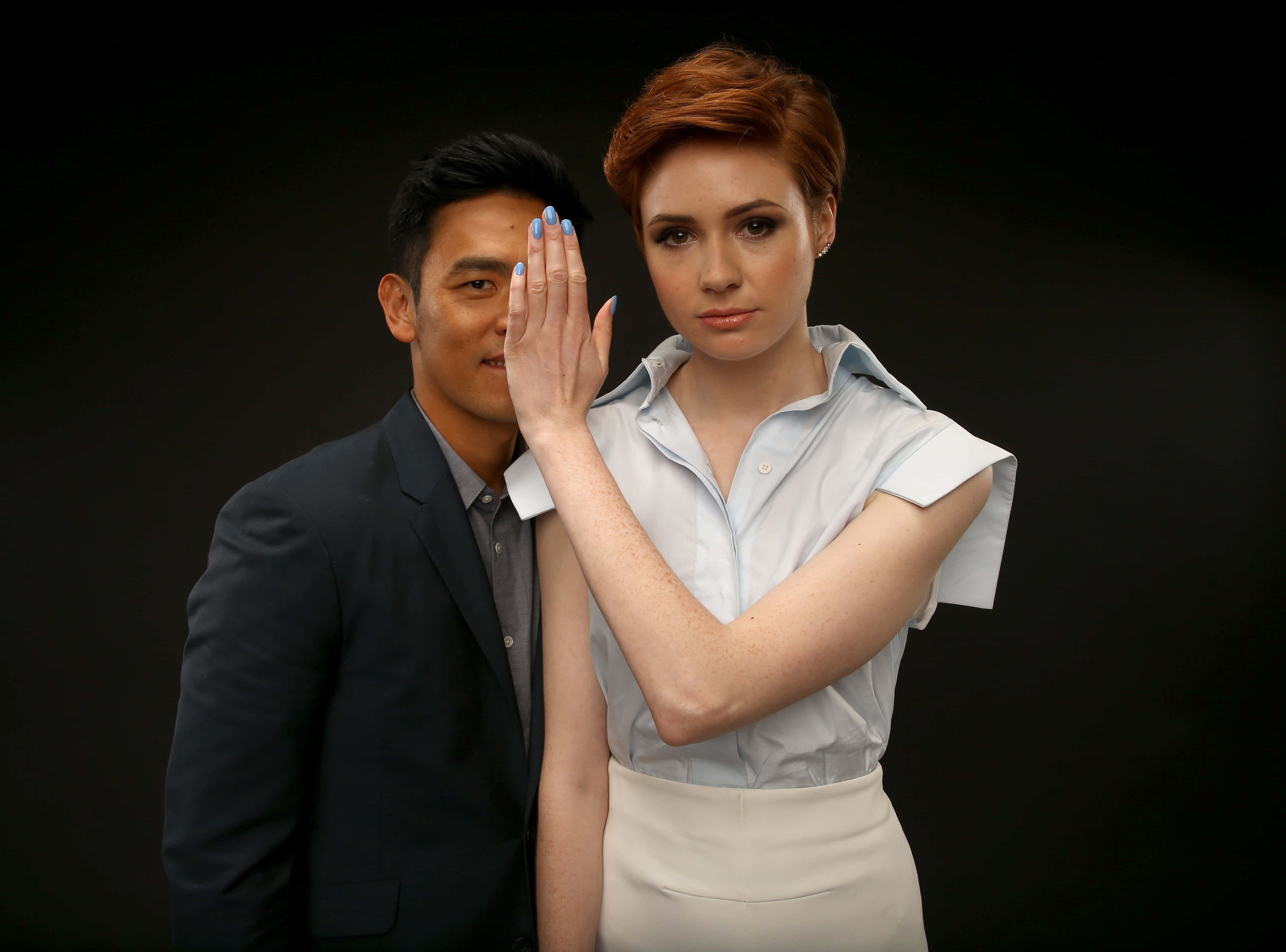 John Cho 桌布 壁紙 — 一位紅髮、塗著藍色指甲油的女士，在黑色背景前擺姿勢時，用手遮住了一位男士的嘴。
