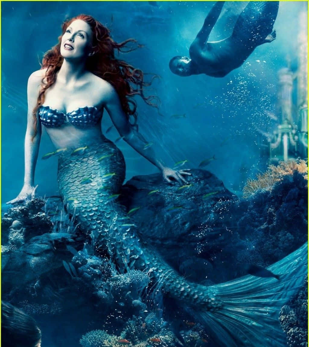 Mermaid Real Life 桌布 壁紙 — 一位紅髮、帶有鱗片尾巴的美人魚優雅地坐在水下岩石上，而一名潛水員在藍色海洋深處漂浮在上方。