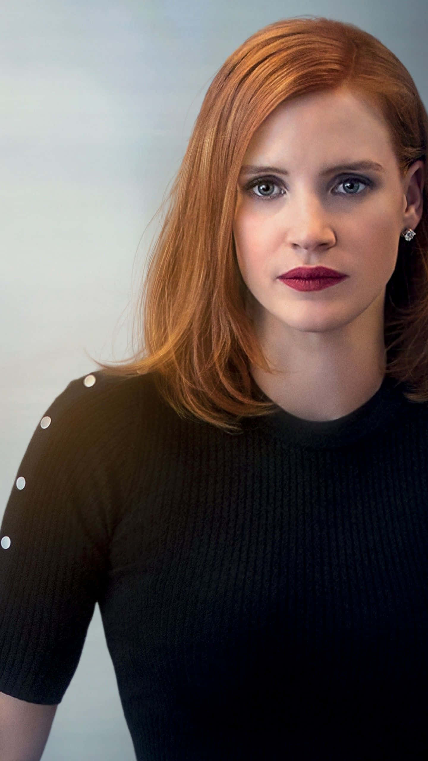 jessica chastain 桌布 壁紙 — 一位紅髮、紅唇大膽的女性，穿著帶白色鈕扣的黑色羅紋上衣，直視鏡頭。