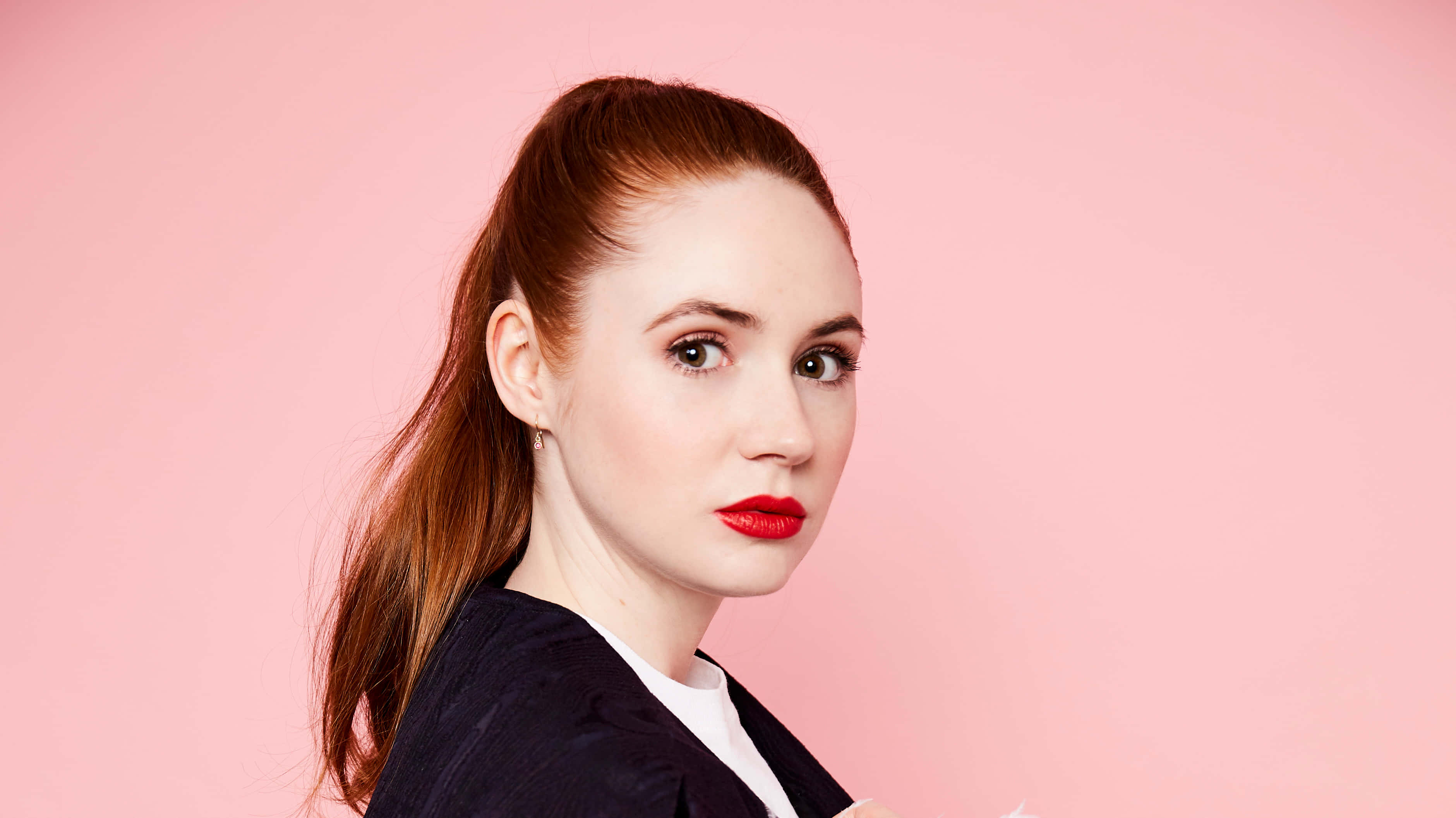 karen gillan 桌布 壁紙 — 一位紅髮、紅唇大膽的女性在柔和的粉紅色工作室背景下直視鏡頭。