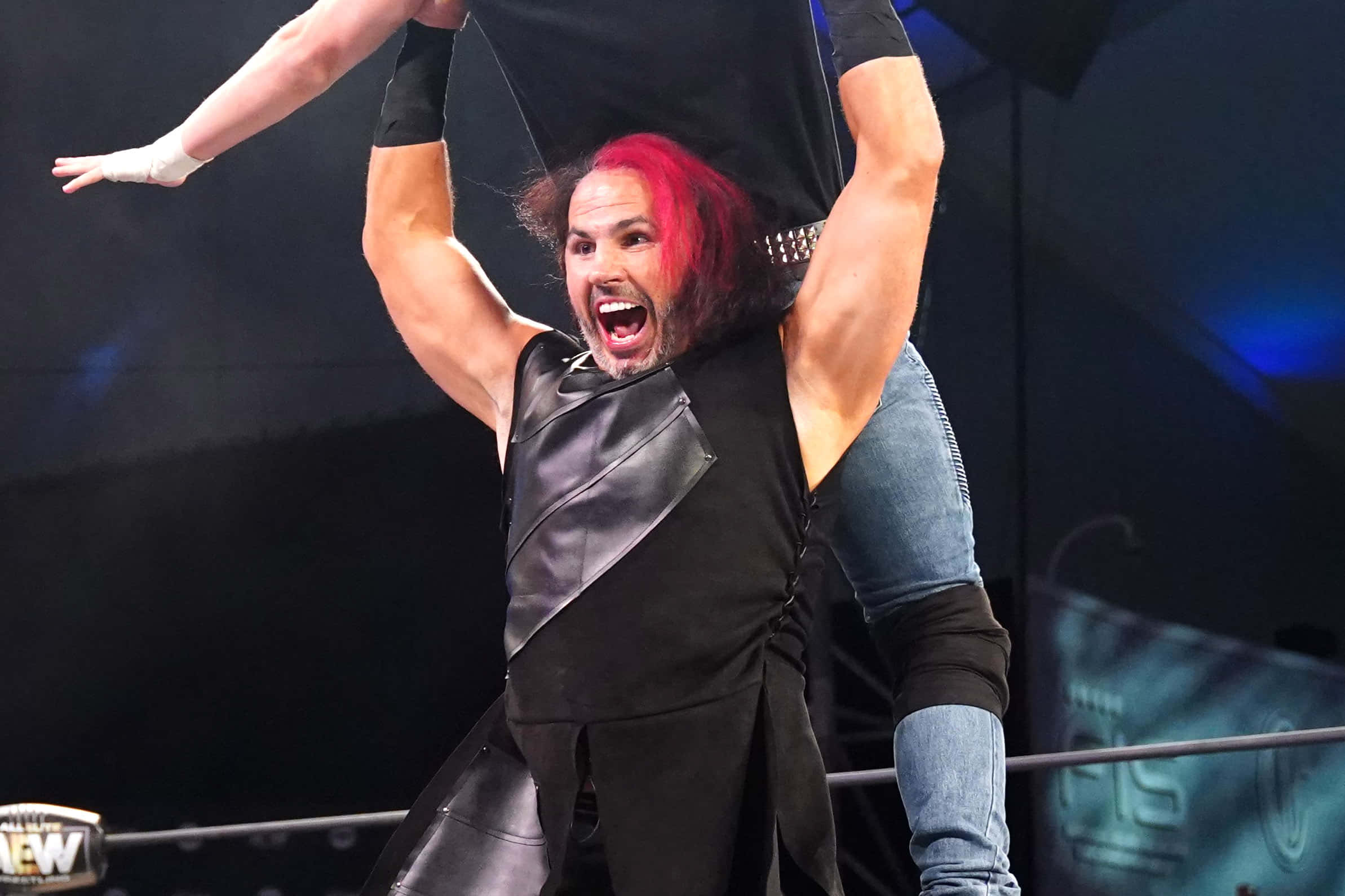 WWE 桌布 壁紙 — 一位紅髮、身穿黑色皮衣的摔角手在明亮的舞台燈光下，在摔角場上勝利地舉起對手。