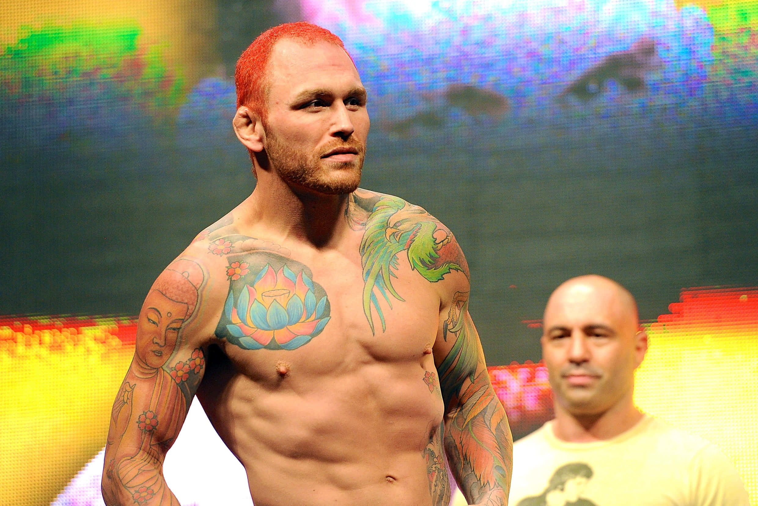 MMA 桌布 壁紙 — 一位紅髮刺青男子在色彩繽紛的抽象背景下，赤裸上身站在充滿活力的舞台燈光下。