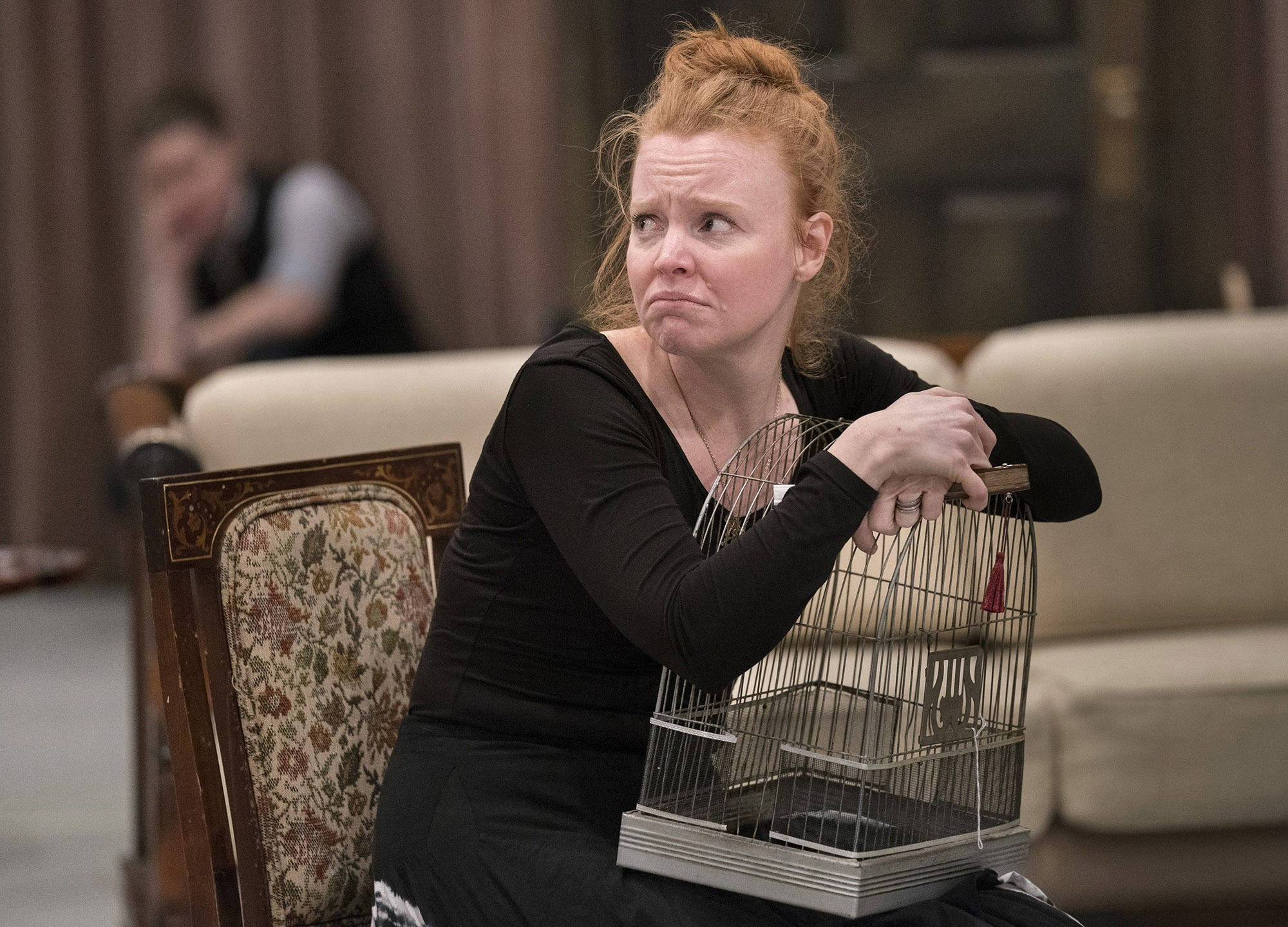 Broadway 桌布 壁紙 — 一位紅髮女士坐在椅子上，手持一個空鳥籠，表情若有所思。