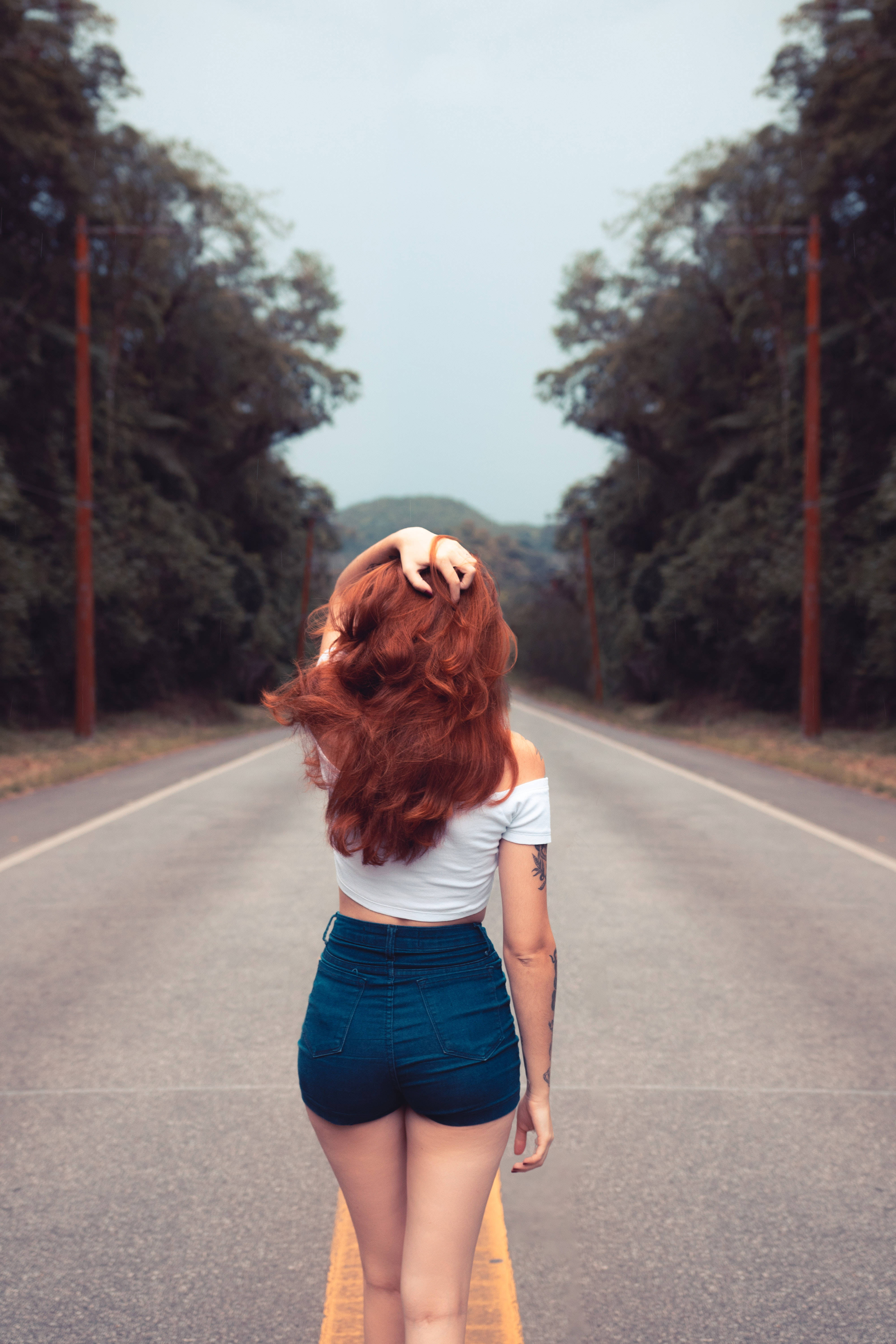 walking away 桌布 壁紙 — 一位紅髮女子站在森林地區的道路上，一手撥弄頭髮，向前凝望。