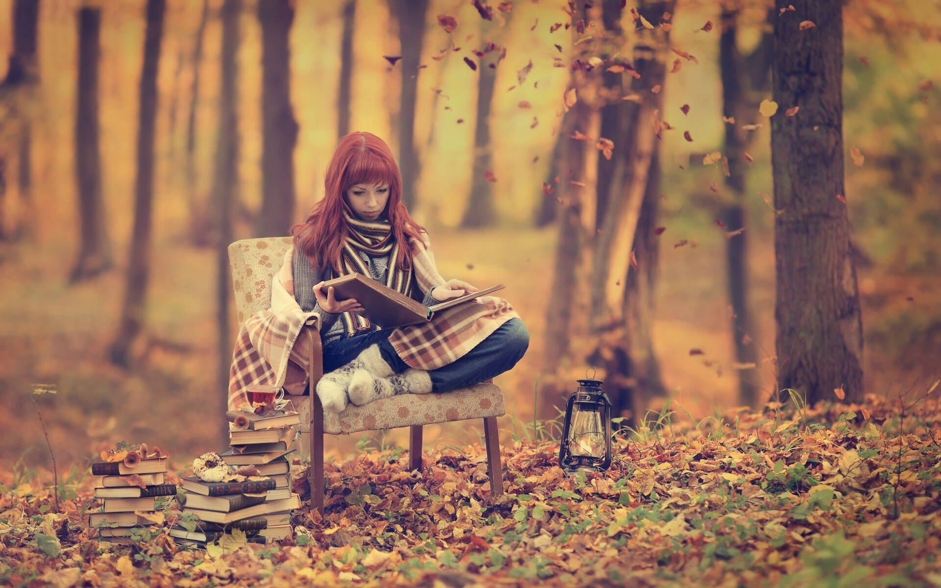 Reading 桌布 壁紙 — 一位紅髮女子裹著格紋毯，坐在森林中被飄落的秋葉和書堆環繞的椅子上看書。