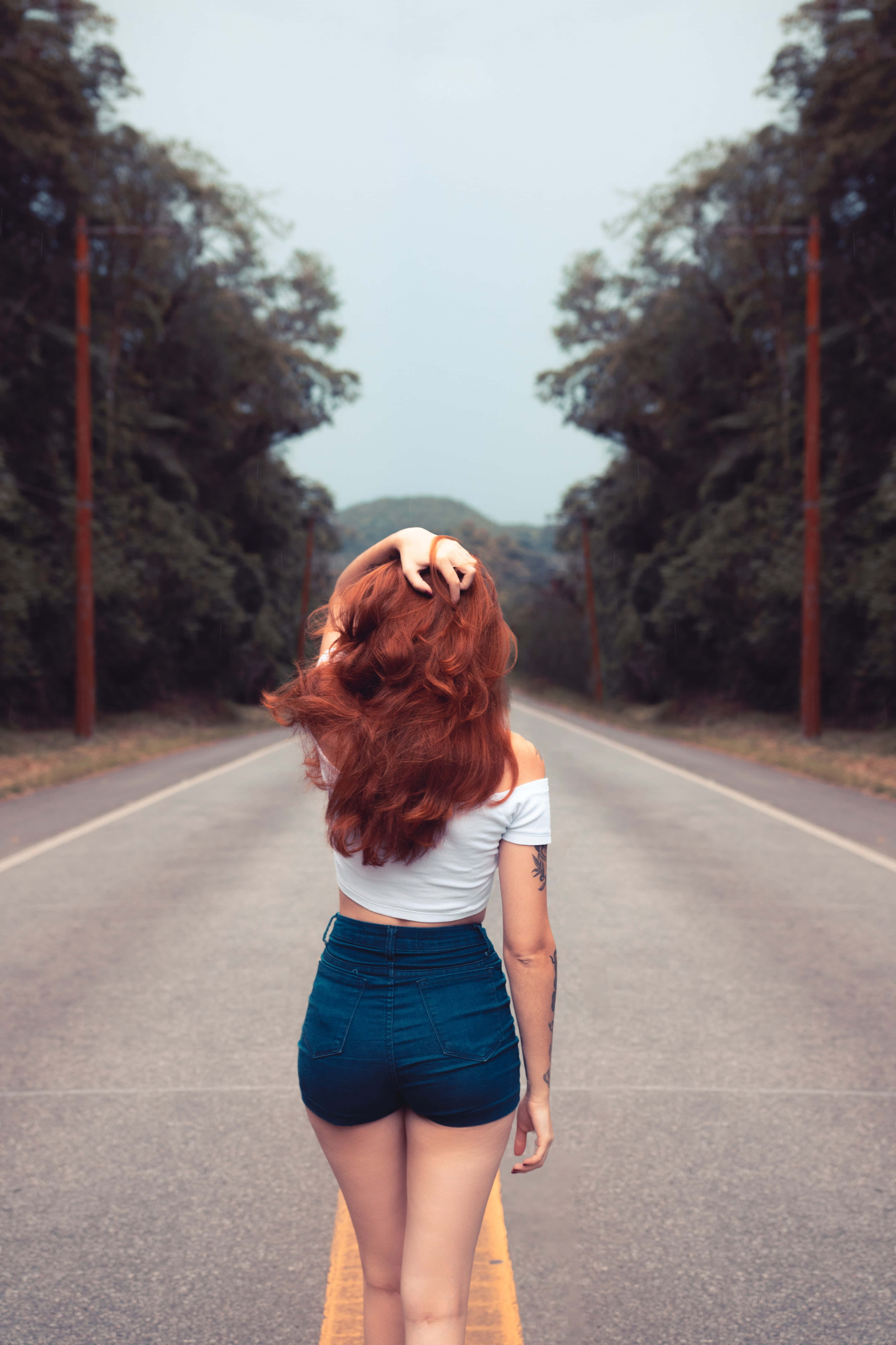 Road 桌布 壁紙 — 一位紅髮女子走在樹木成蔭的道路上，身穿白色露臍上衣和牛仔短褲。