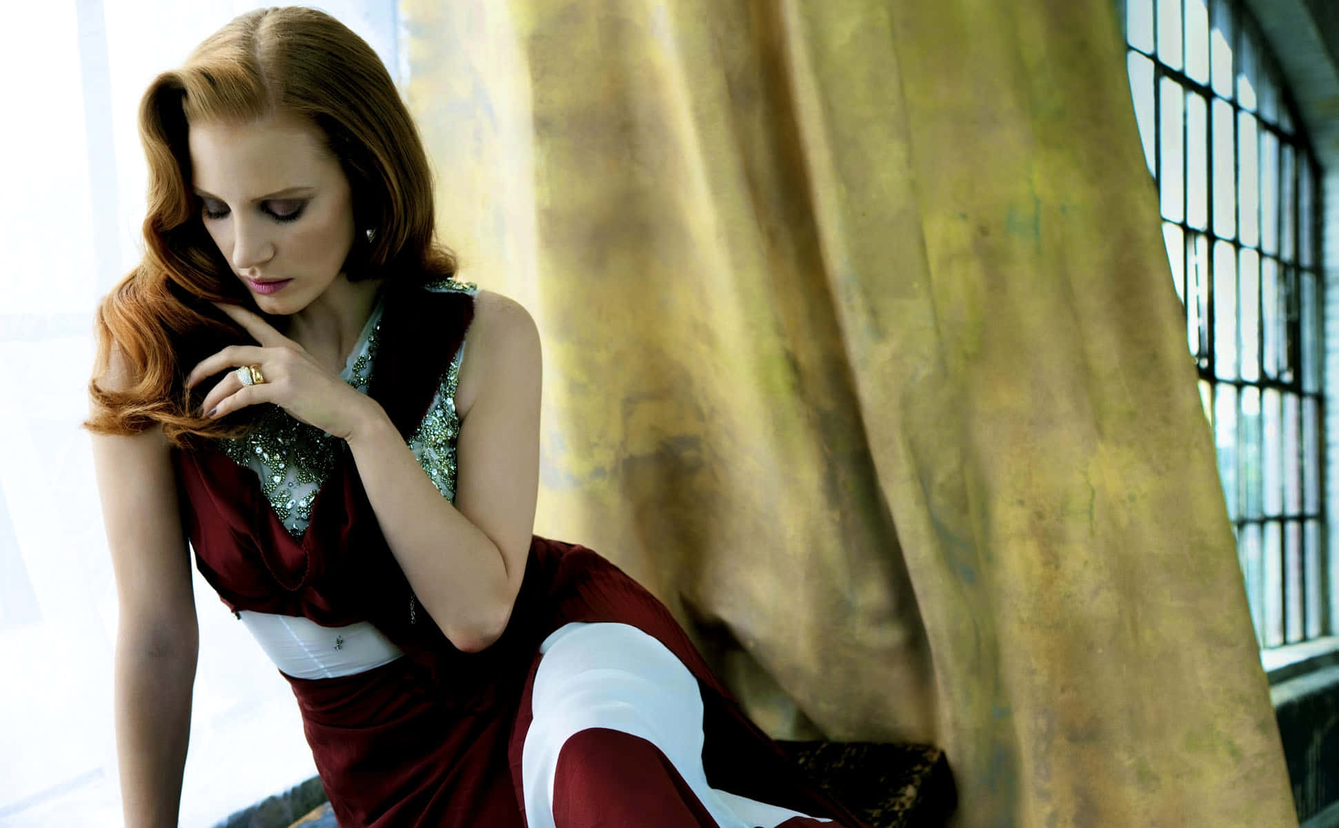 jessica chastain 桌布 壁紙 — 一位紅髮女子身穿栗色和白色連衣裙，坐在金色窗簾的窗邊沉思。
