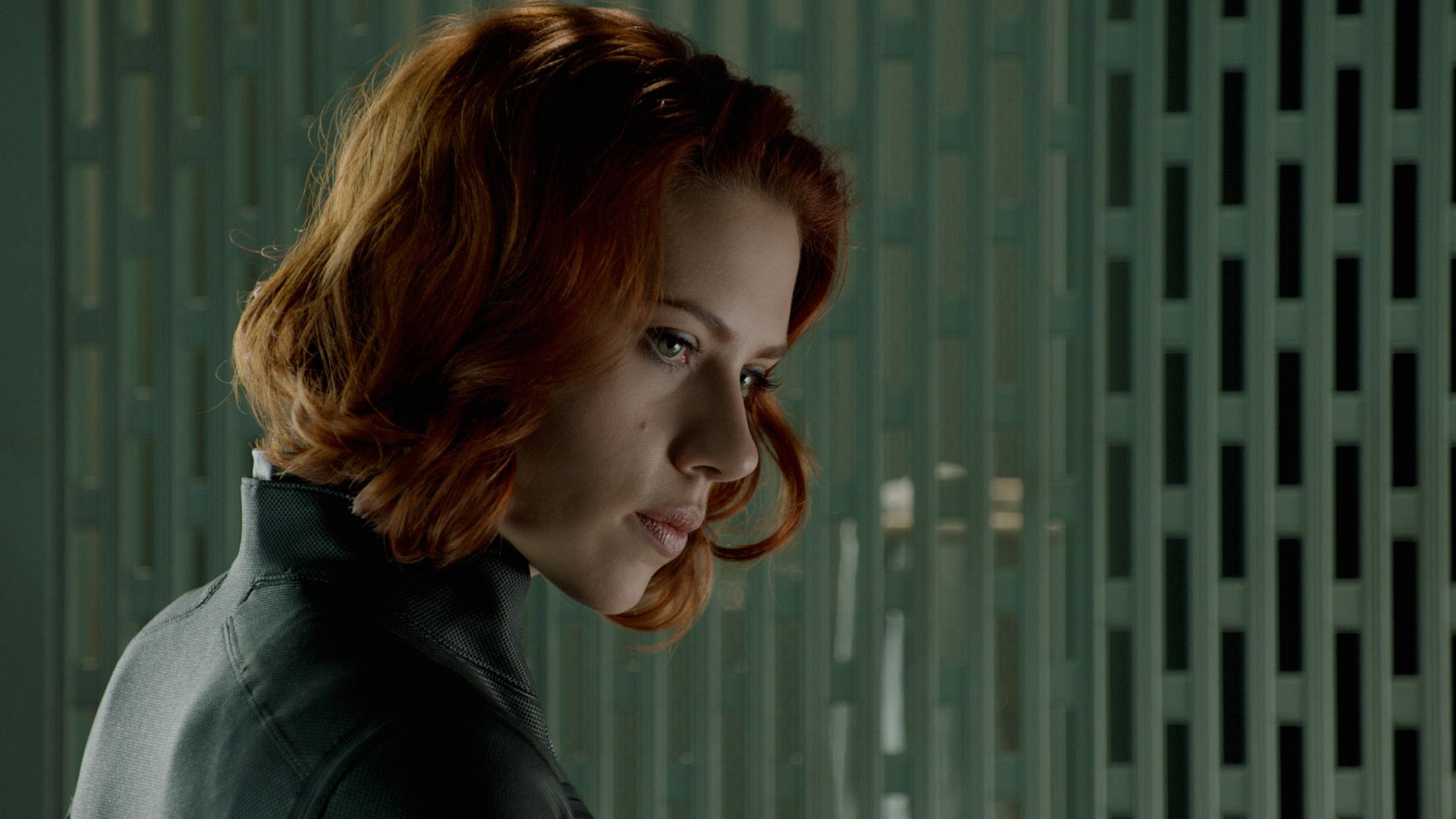Scarlett Johansson Black Widow 桌布 壁紙 — 一位紅髮女子身穿深色外套，對著綠色板條牆若有所思地凝視。