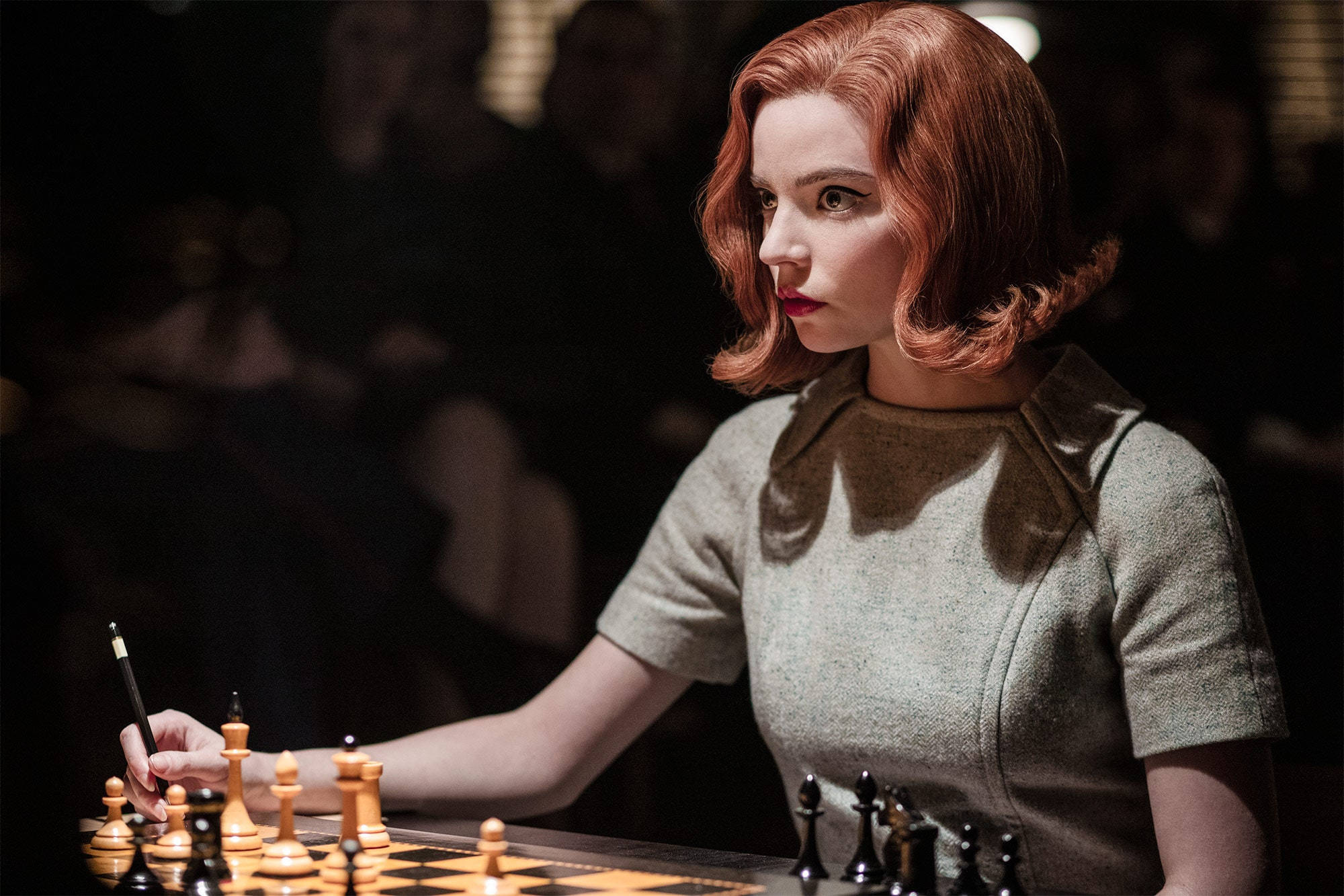 西洋棋 桌布 壁紙 — 一位紅髮女性在戲劇性燈光下專注於西洋棋遊戲，背景有模糊的觀眾。