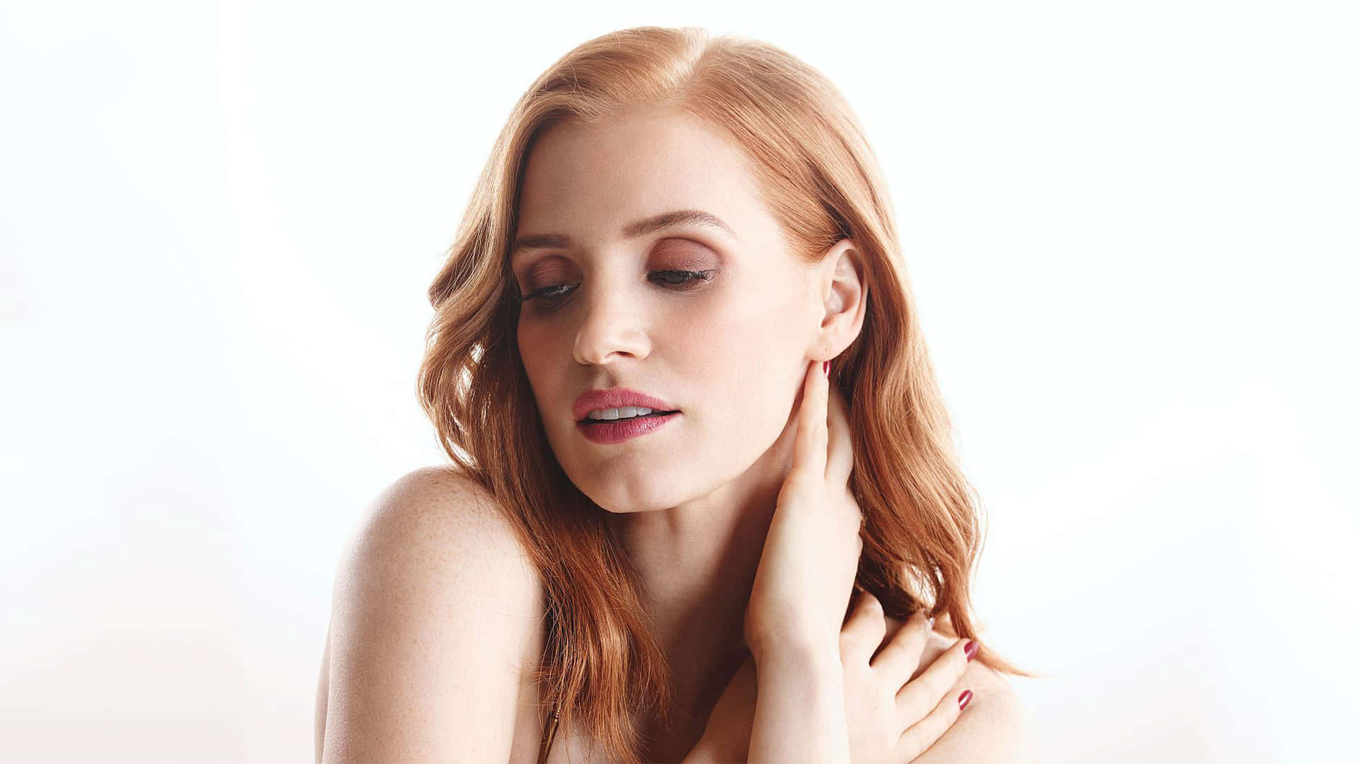 jessica chastain 桌布 壁紙 — 一位紅髮女性在柔軟的白色背景前輕輕觸碰頸部。