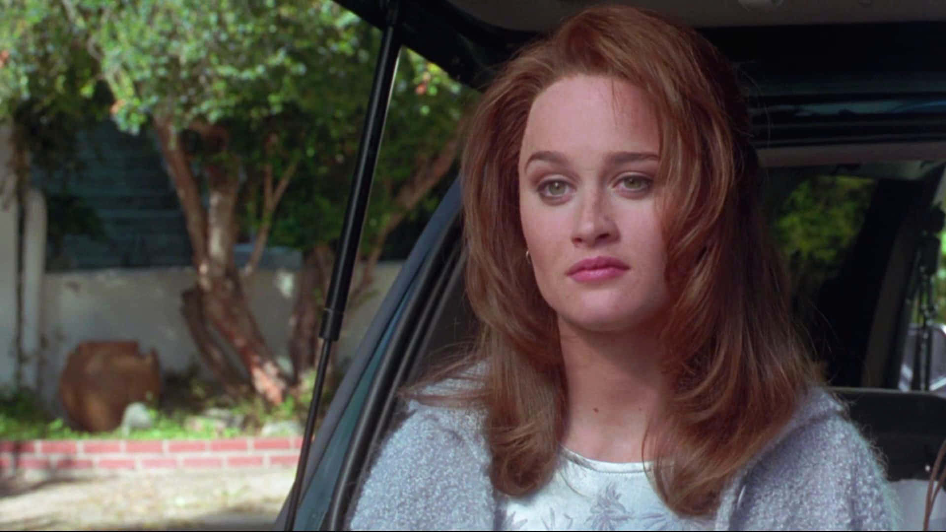 Robin Tunney 桌布 壁紙 — 一位紅髮女性坐在車內，以嚴肅的表情凝視前方，背景是綠樹和磚牆。