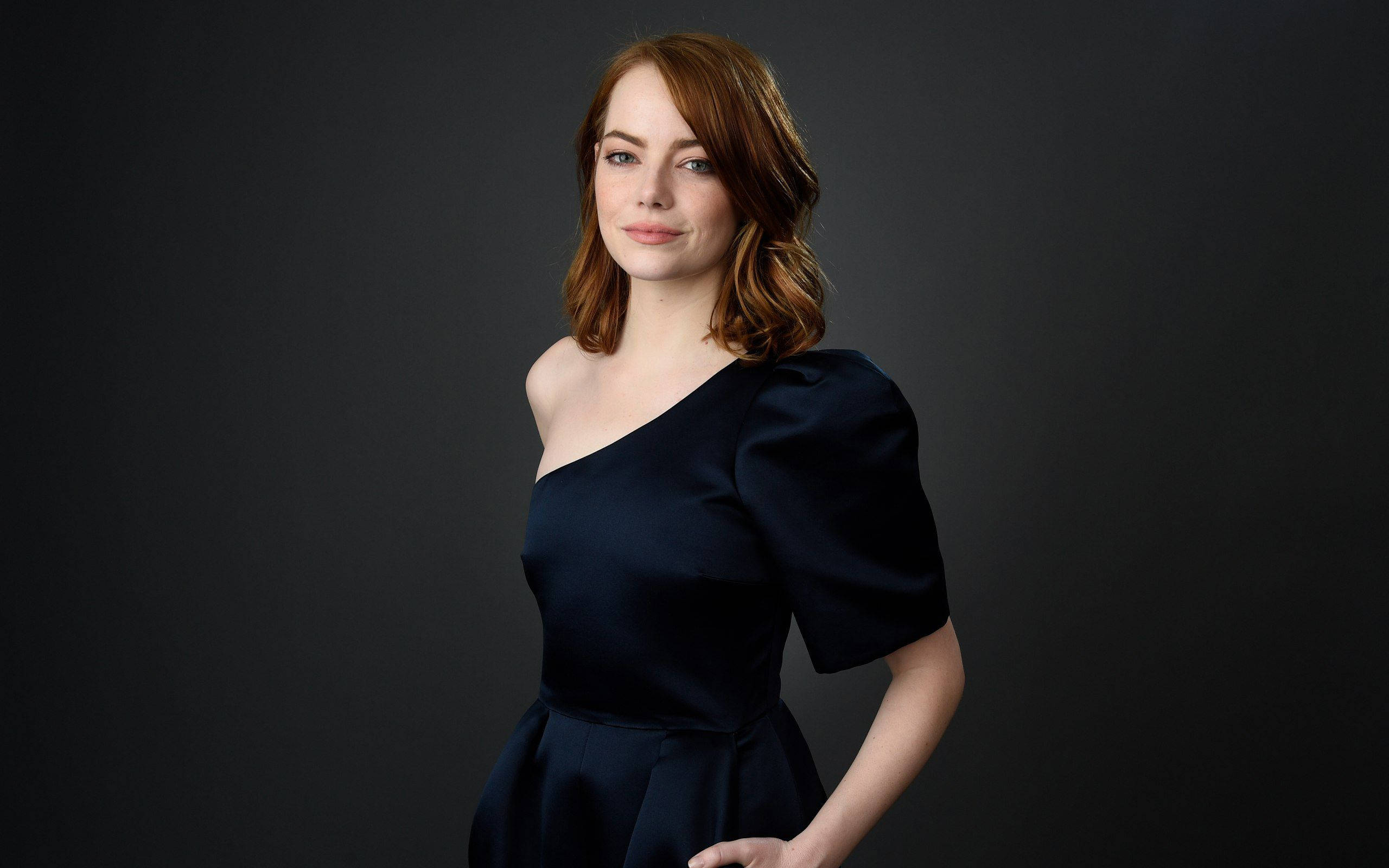 Emma 桌布 壁紙 — 一位紅髮女性穿著海軍藍單肩連衣裙，背景為深灰色攝影棚。