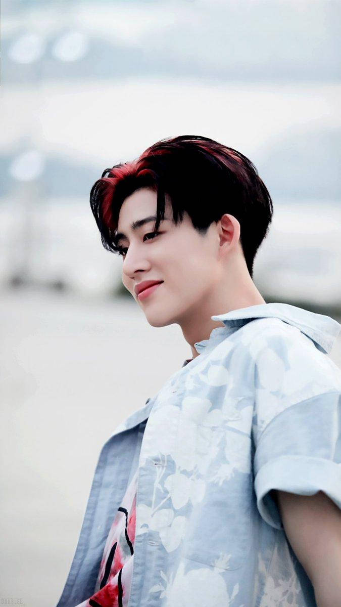 kim hanbin 桌布 壁紙 — 一位紅髮尖端的年輕男子穿著淺藍色花卉襯衫，在模糊的海岸背景下溫柔微笑。