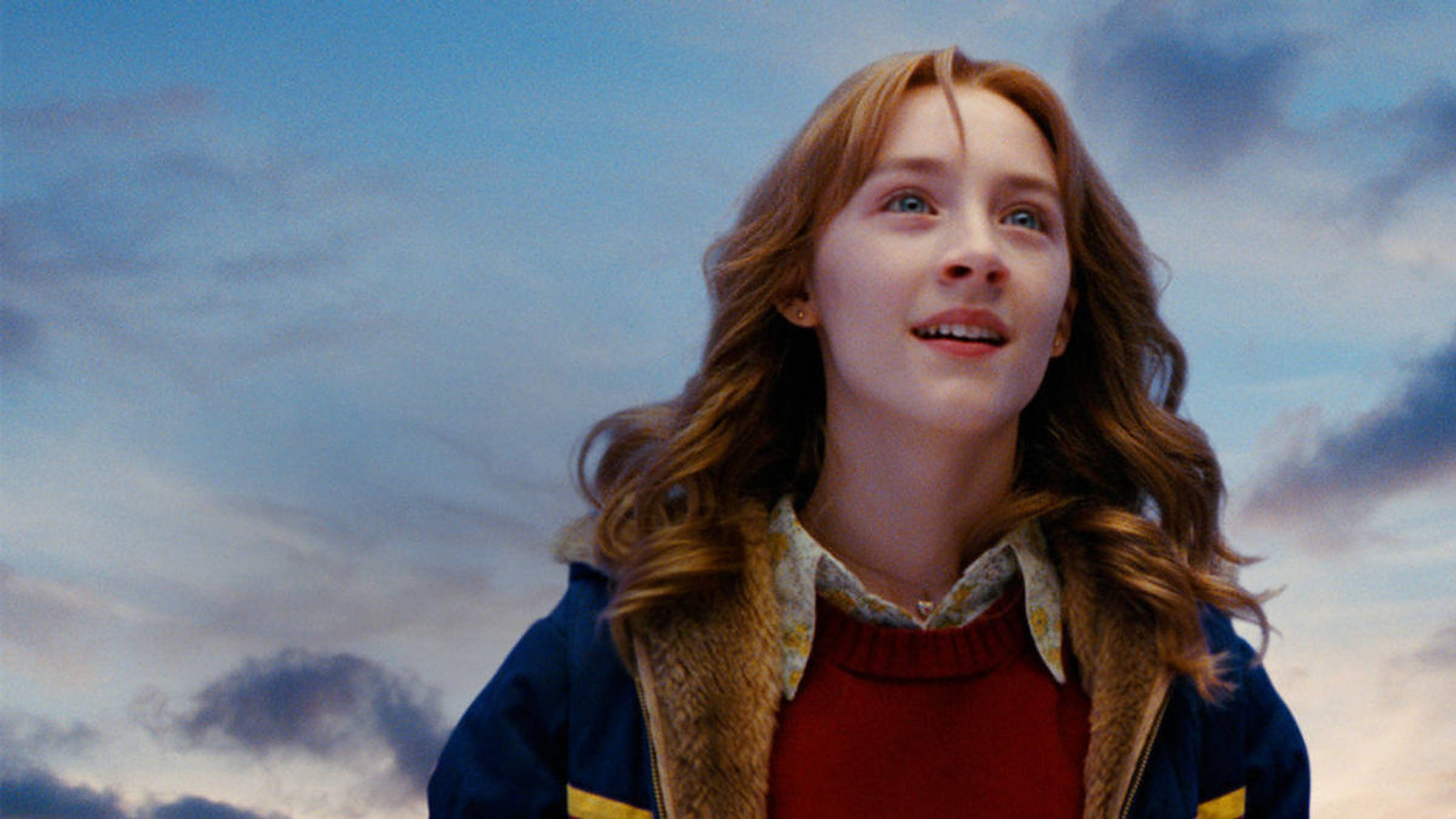 Saoirse Ronan 桌布 壁紙 — 一位紅髮年輕女子在點綴著縷縷白雲的柔和藍天下，帶著驚奇向上凝望。
